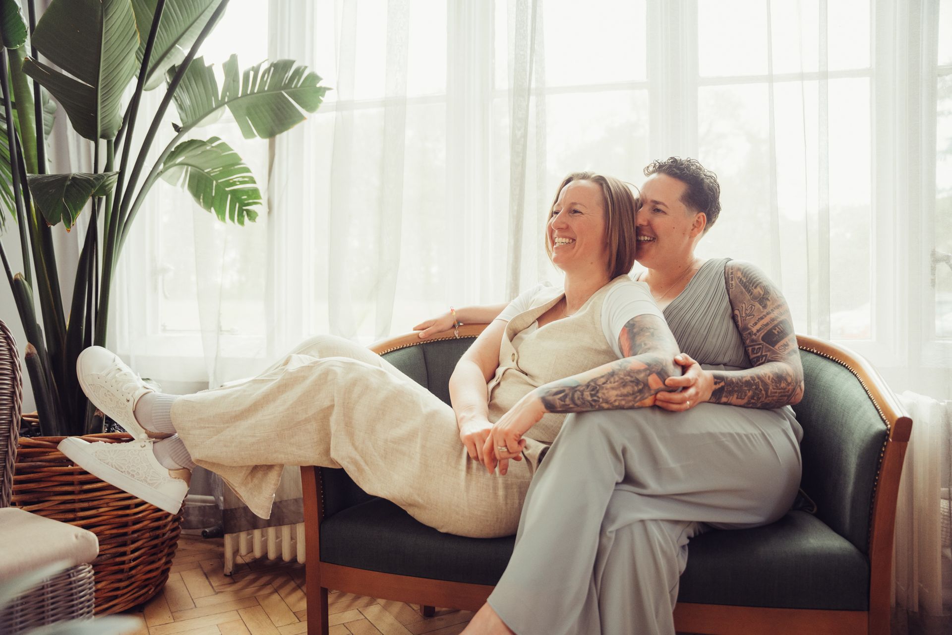 Two women are sitting on a couch holding hands and smiling.