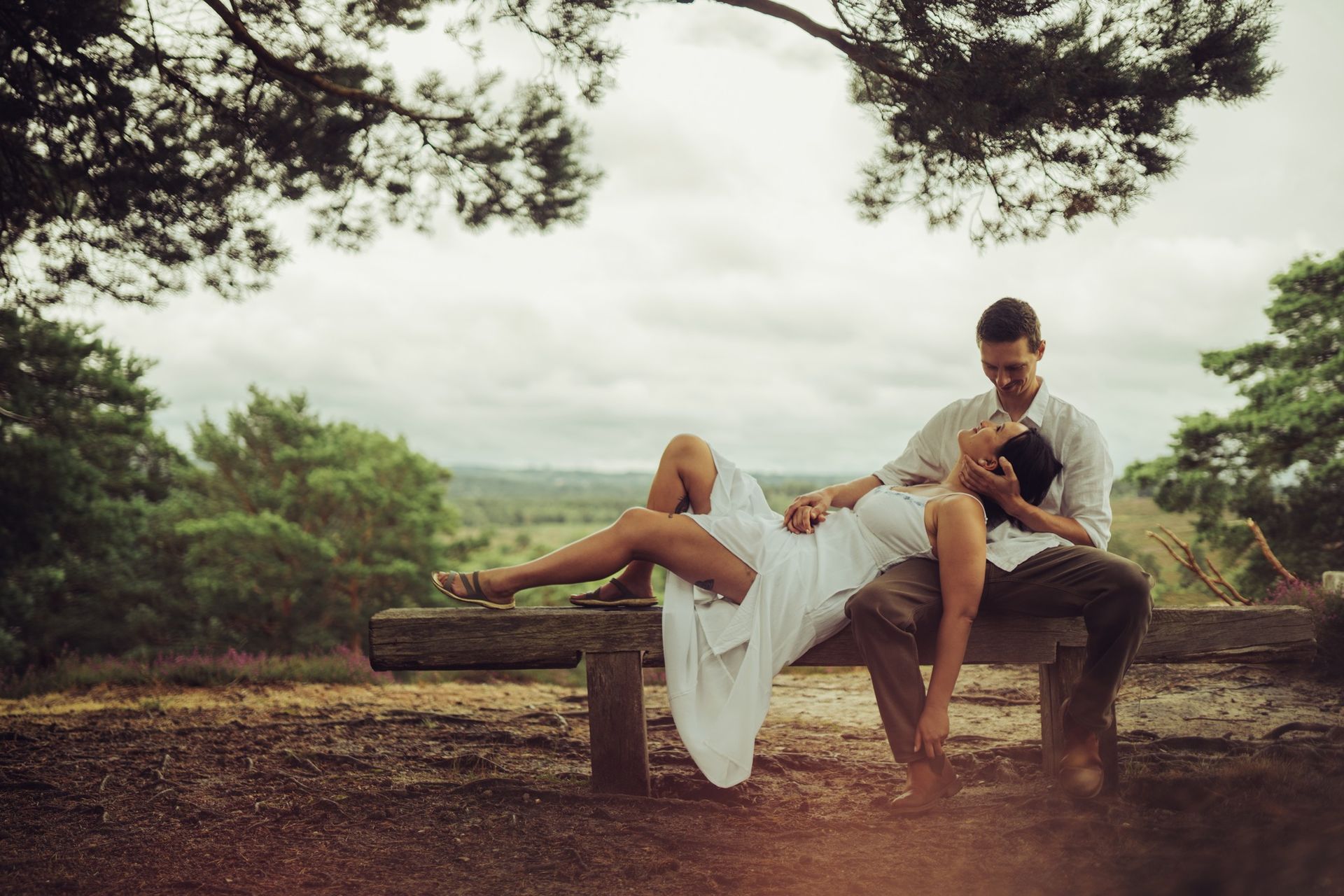 A man and a woman are sitting on a bench under a tree.