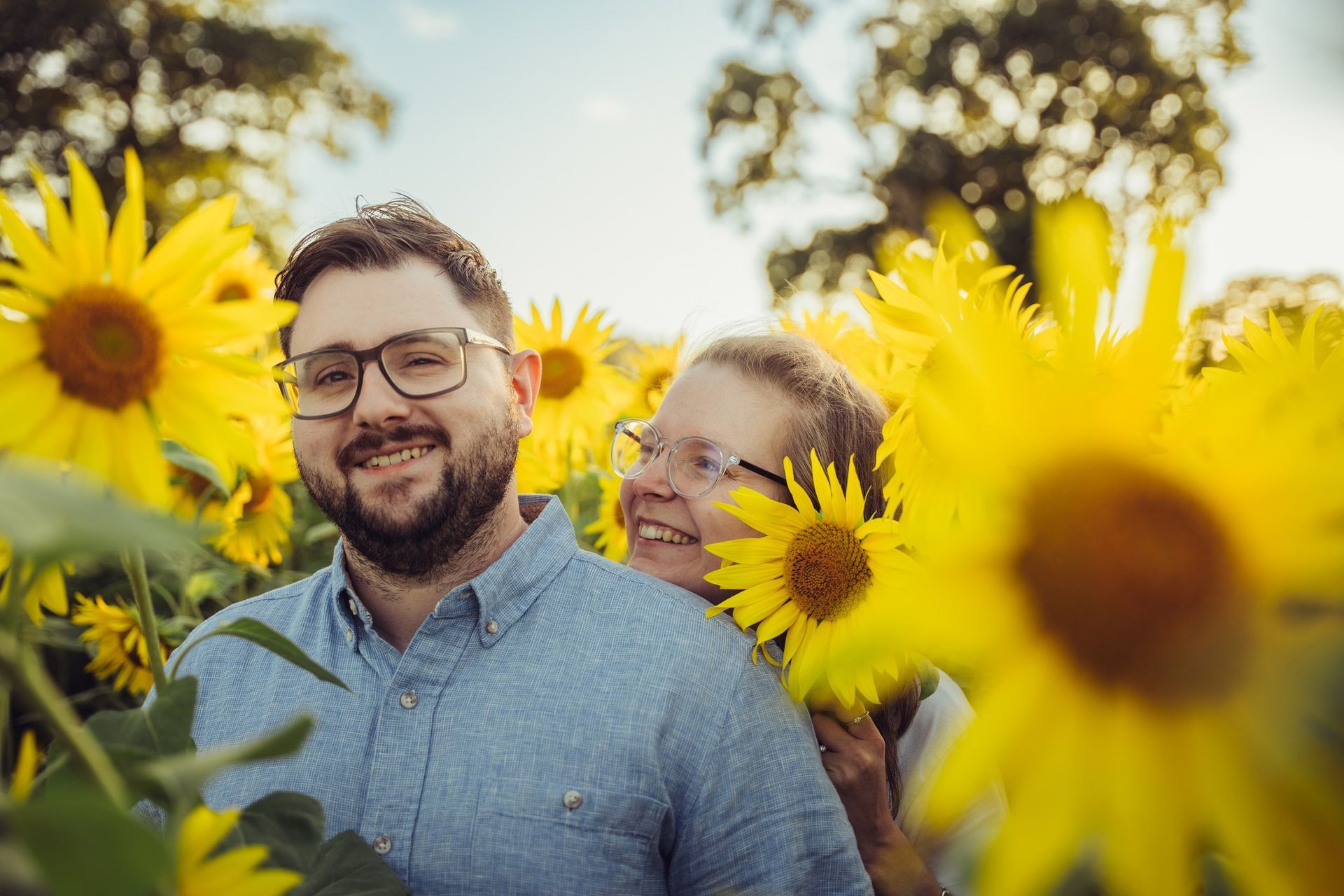 A man and a woman are standing in a field of sunflowers.