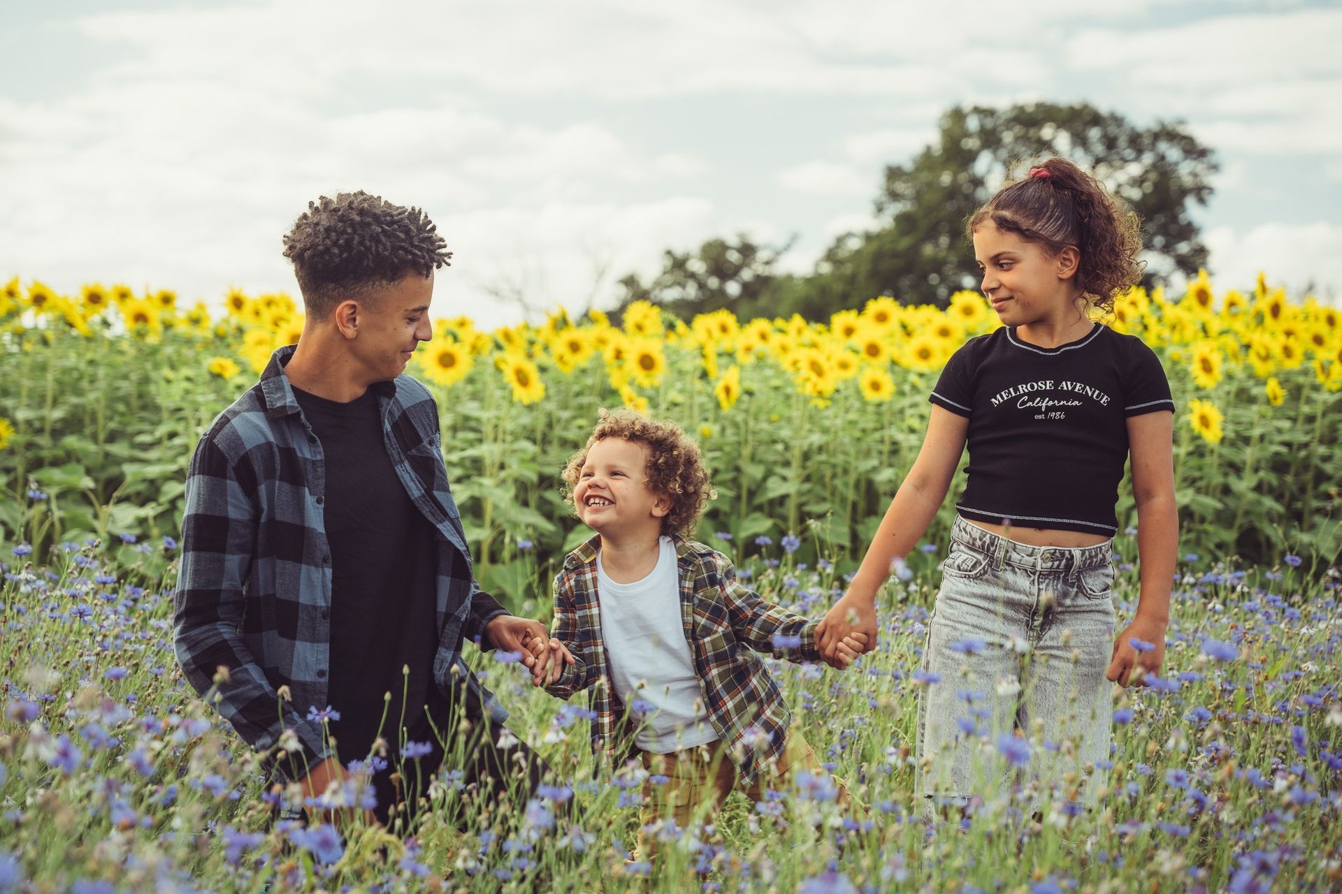 A man and two children are holding hands in a field of sunflowers.