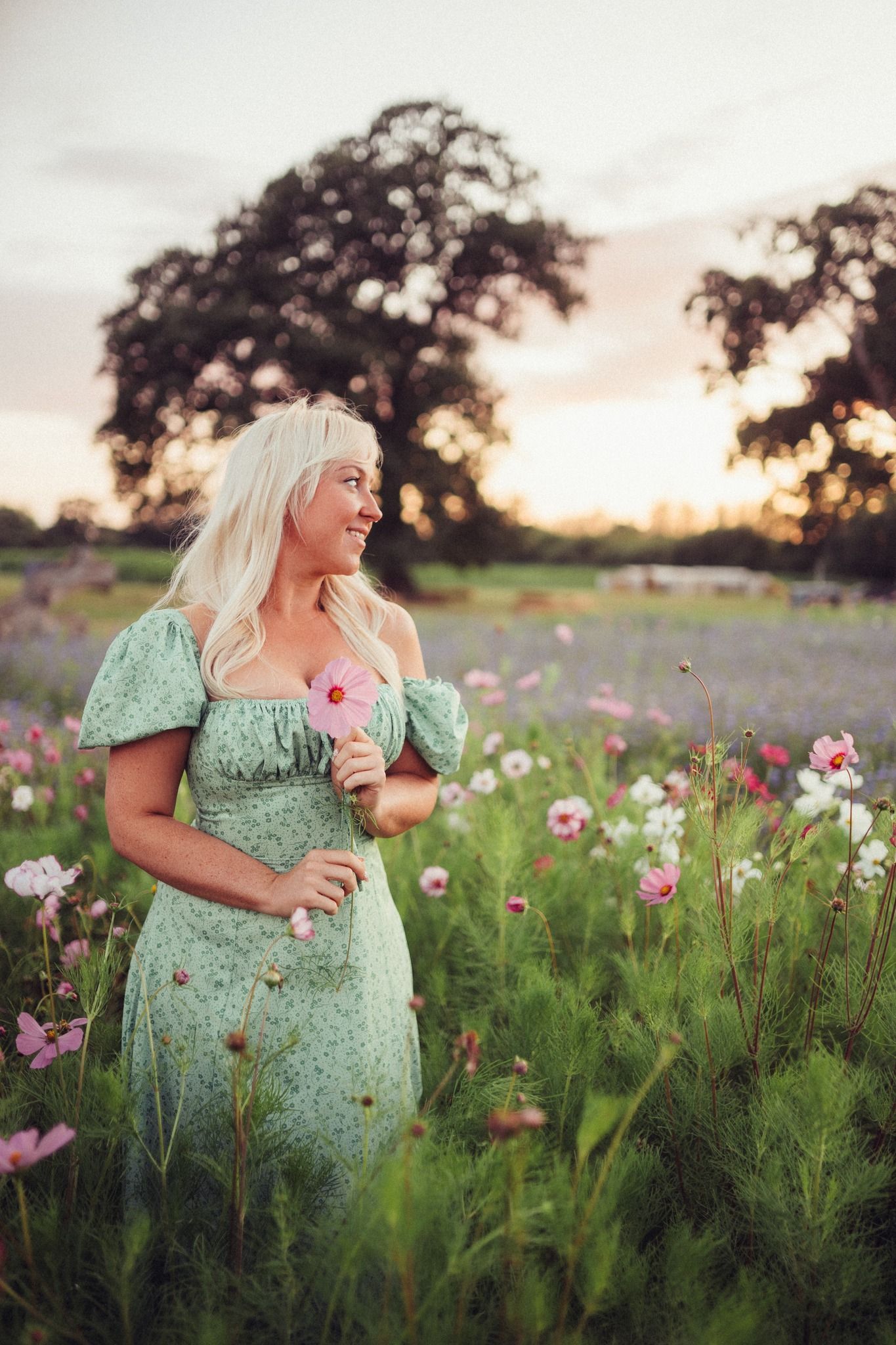 A woman in a green dress is standing in a field of flowers.
