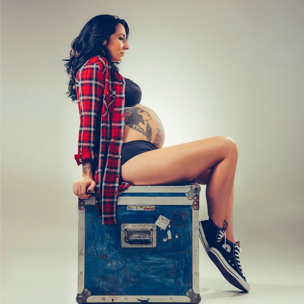 A pregnant woman is sitting on a suitcase with her legs crossed