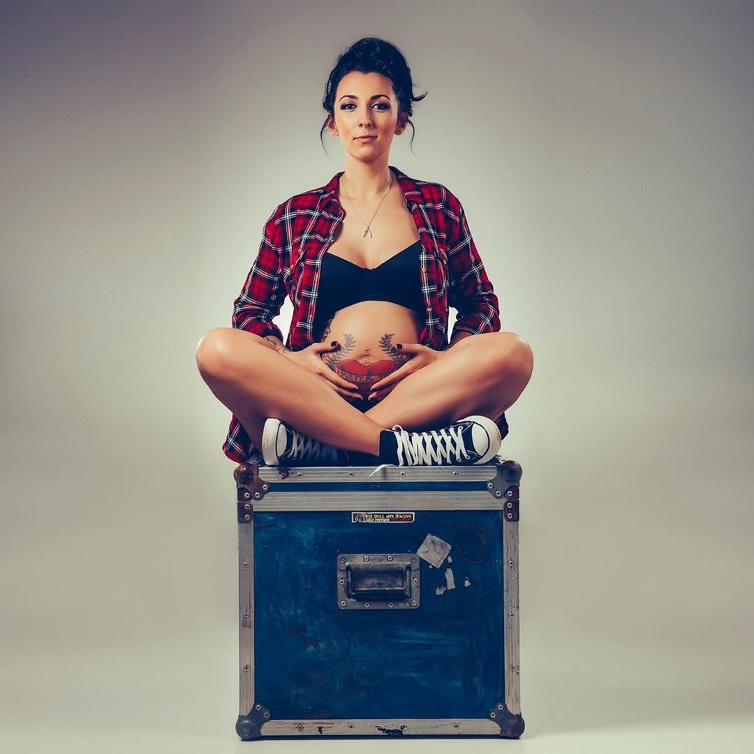 A pregnant woman is sitting on a suitcase with her legs crossed