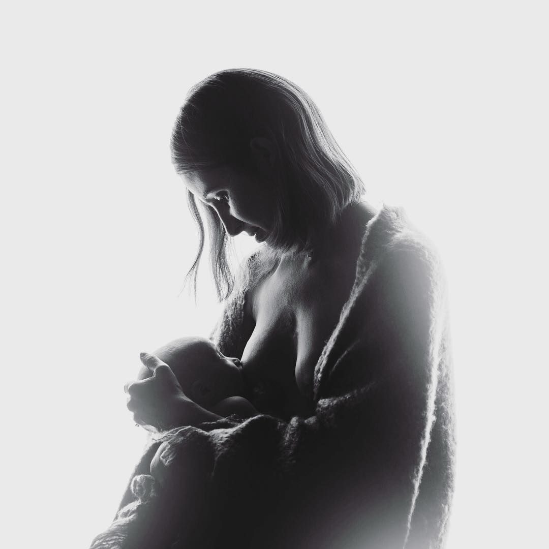 A woman is breastfeeding her baby in a black and white photo.