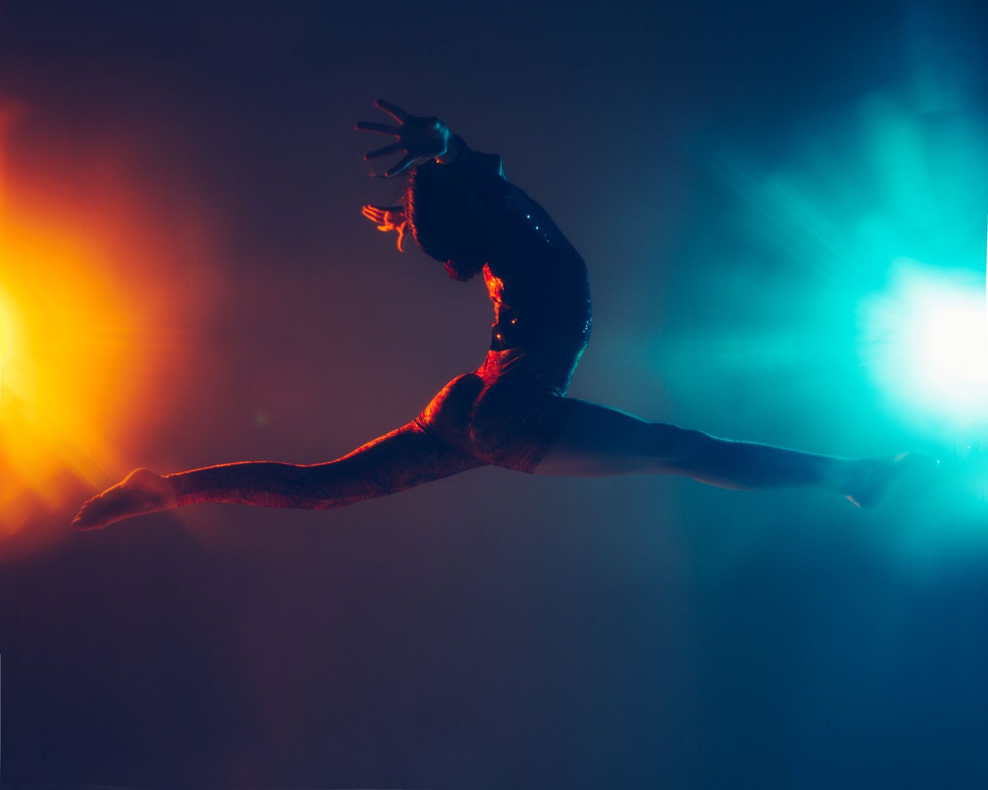 A person is jumping in the air in front of a colorful light.