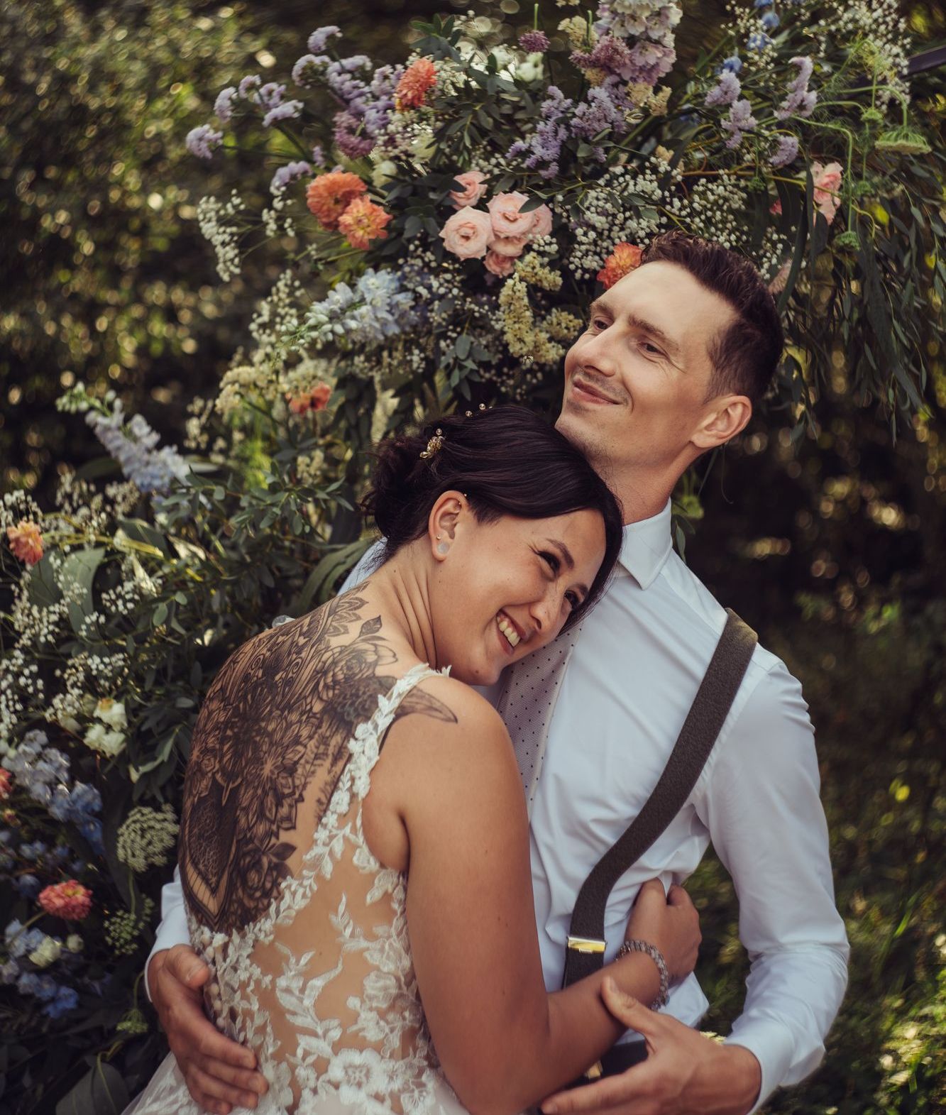 A bride and groom are posing for a picture in front of a flower arch.