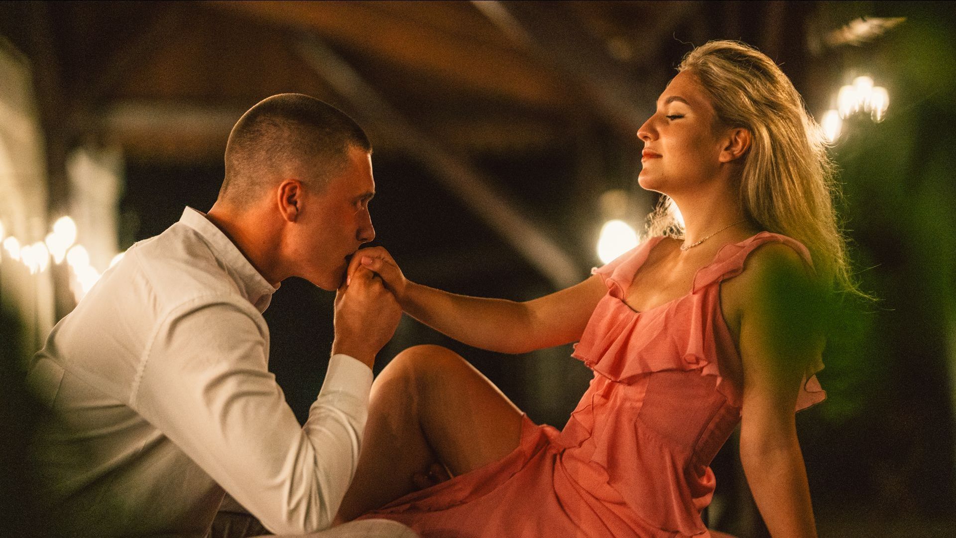 A man is kissing a woman 's hand while she is sitting on the floor.