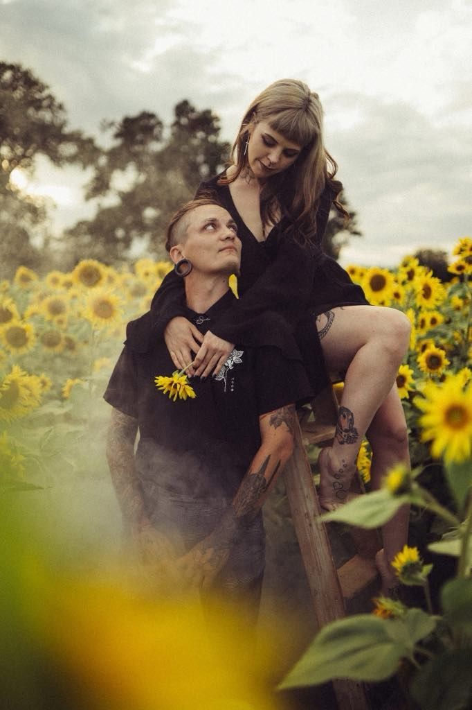 A person is carrying a woman on their back in a field of sunflowers.