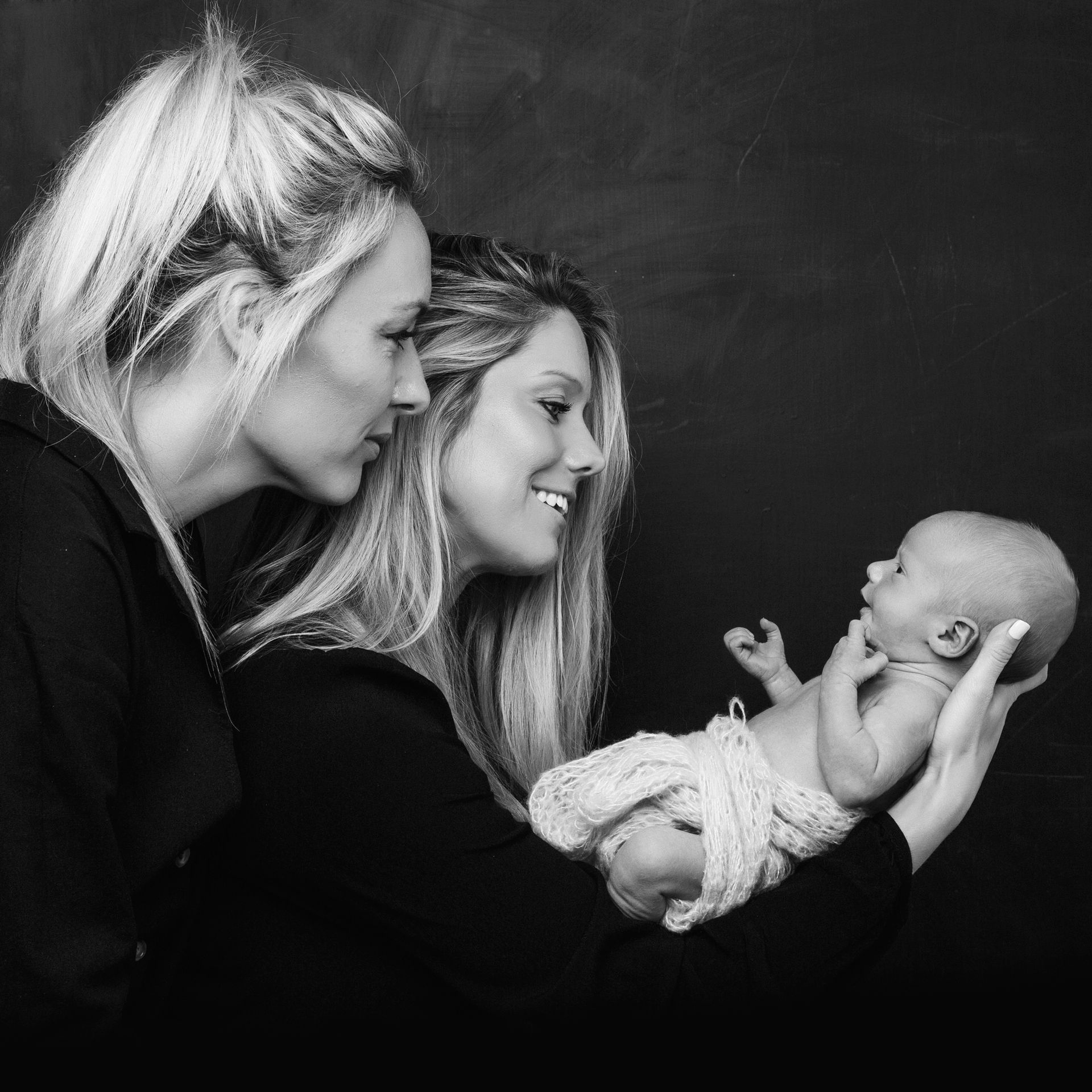 Two women are holding a baby in their arms in a black and white photo.