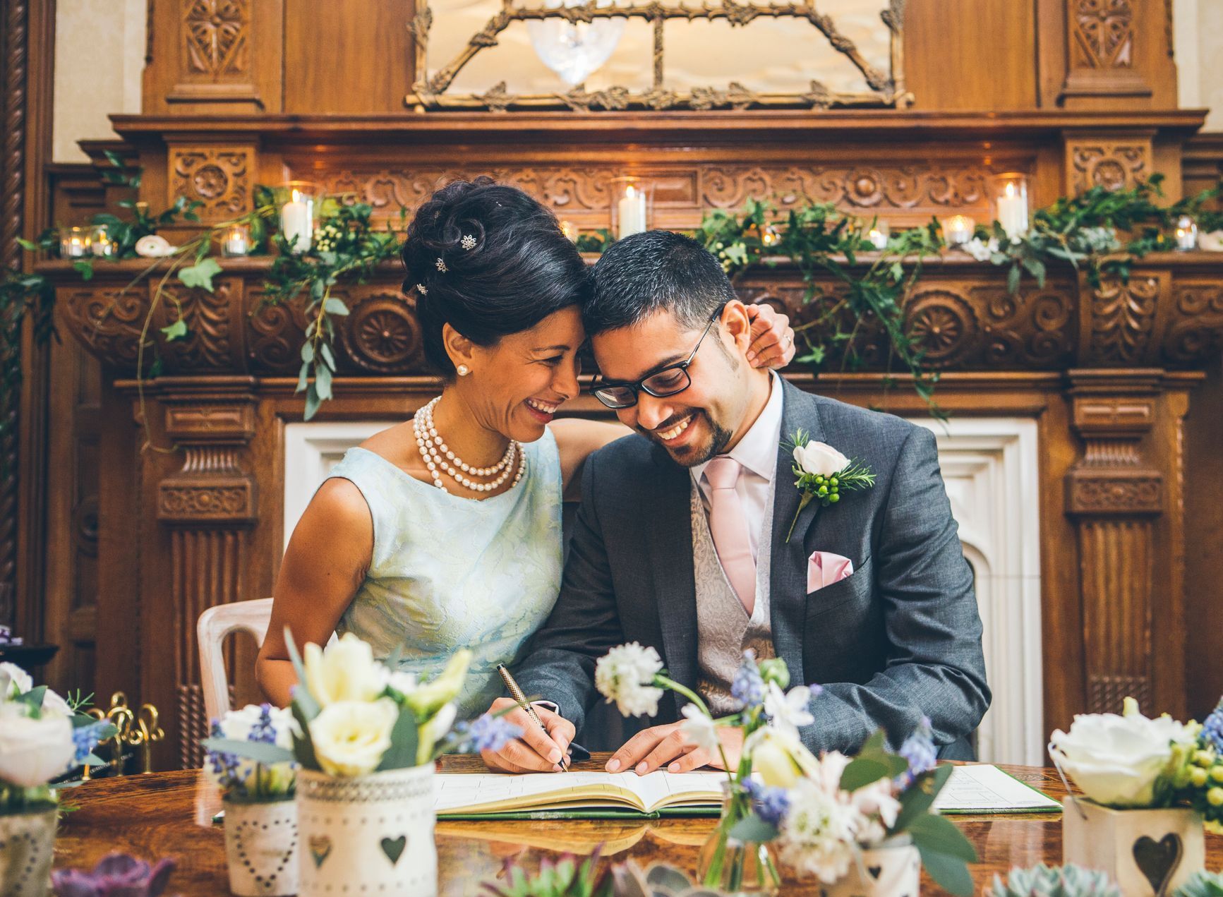 A bride and groom are sitting at a table signing a wedding certificate.