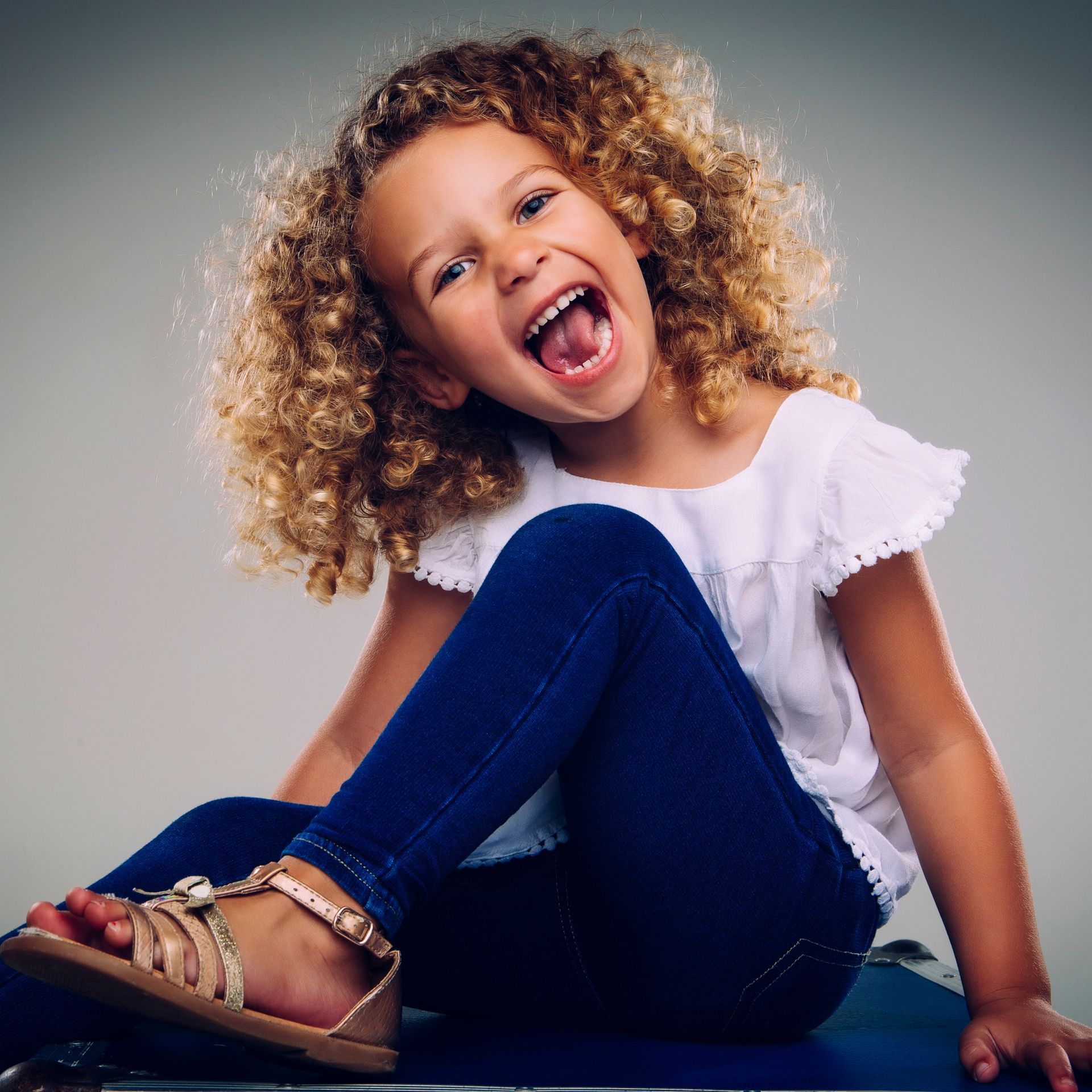 A little girl is sitting next to a cake and balloons