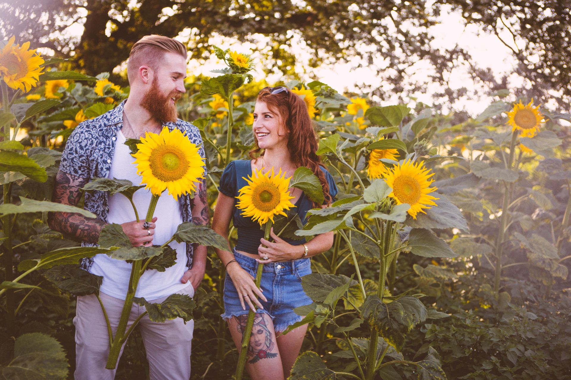 A man and a woman are standing in a field of sunflowers holding sunflowers.
