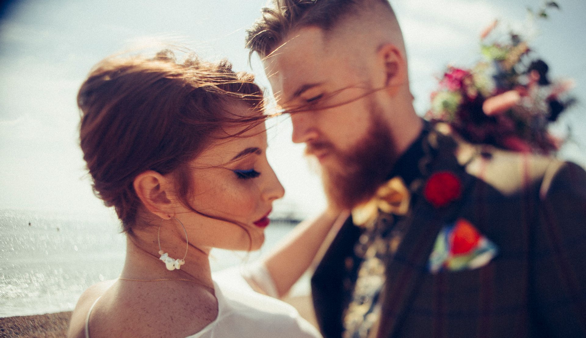 A bride and groom are looking at each other in front of the ocean.