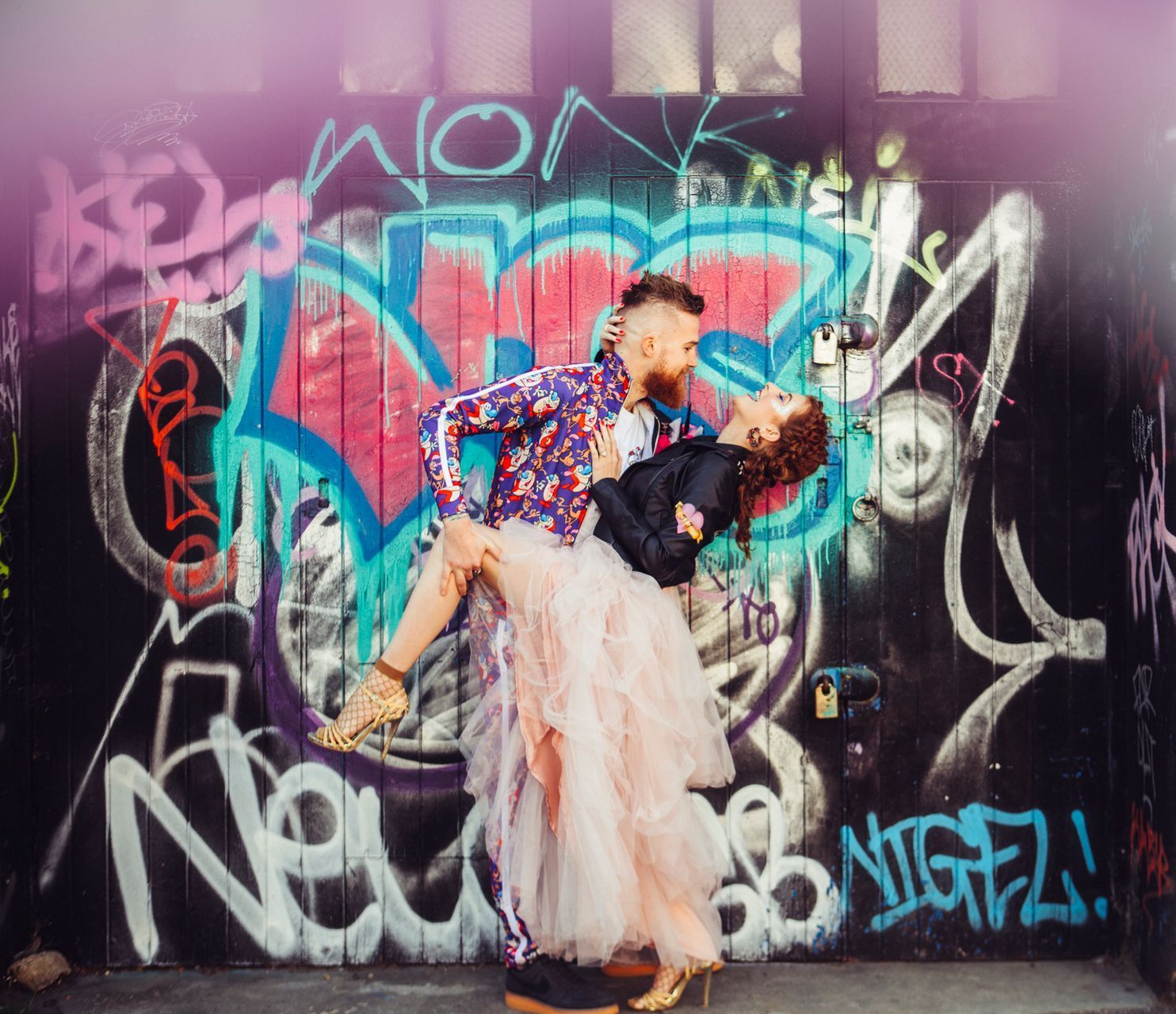 couple stood in front of a wall covered in bright graffiti art