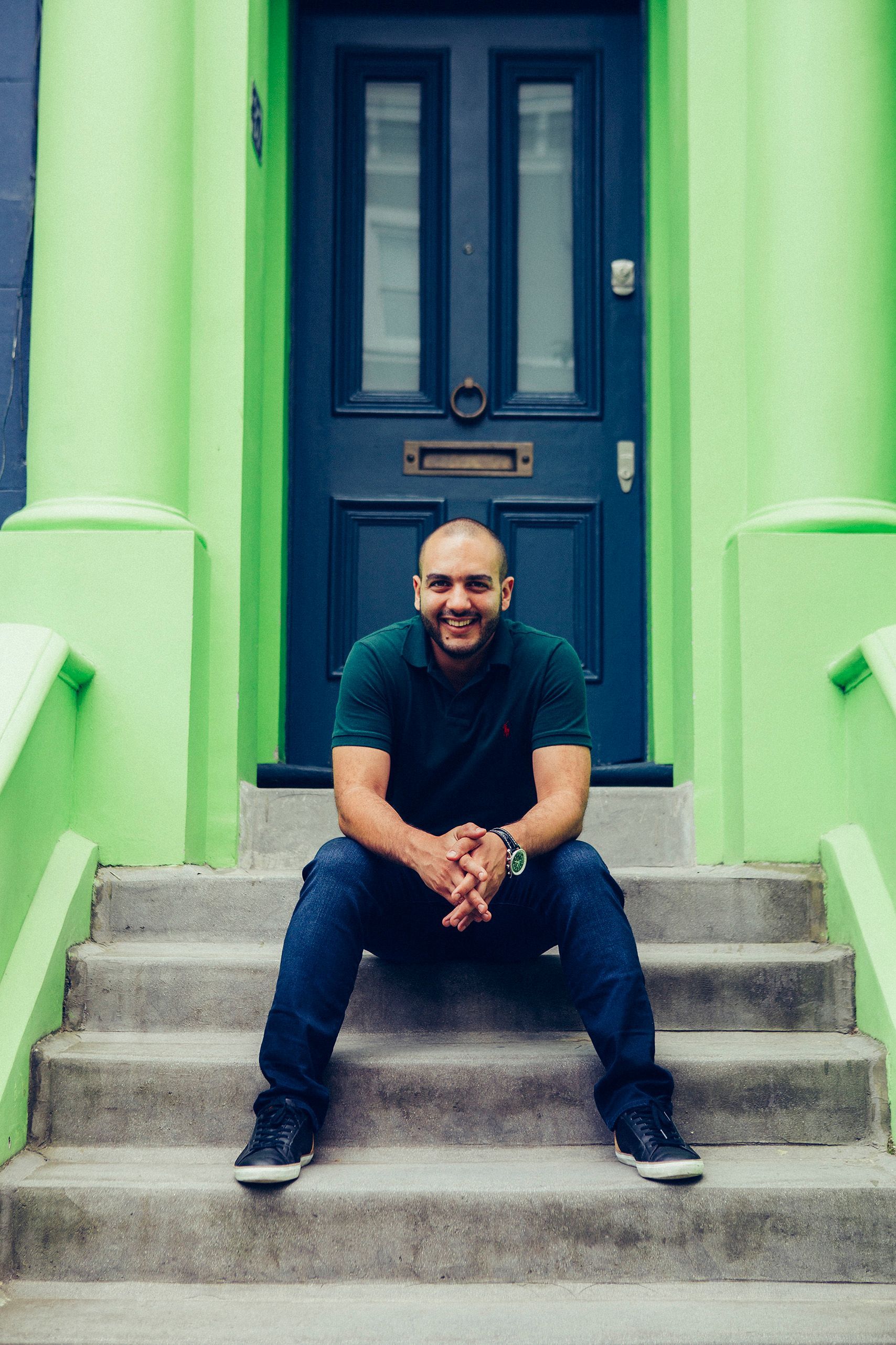 A man is sitting on the steps of a green building.