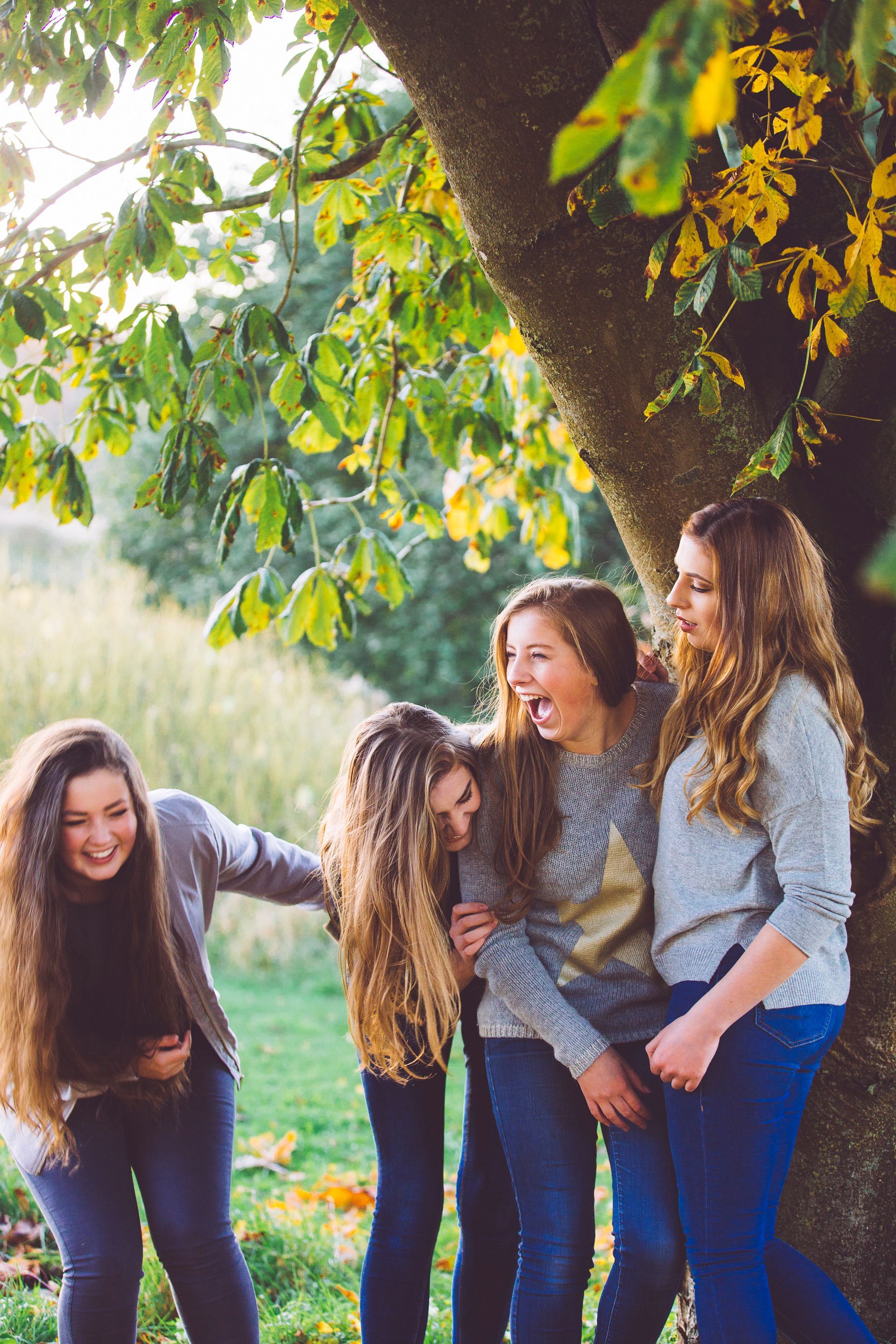 A group of young women are standing next to a tree and laughing.