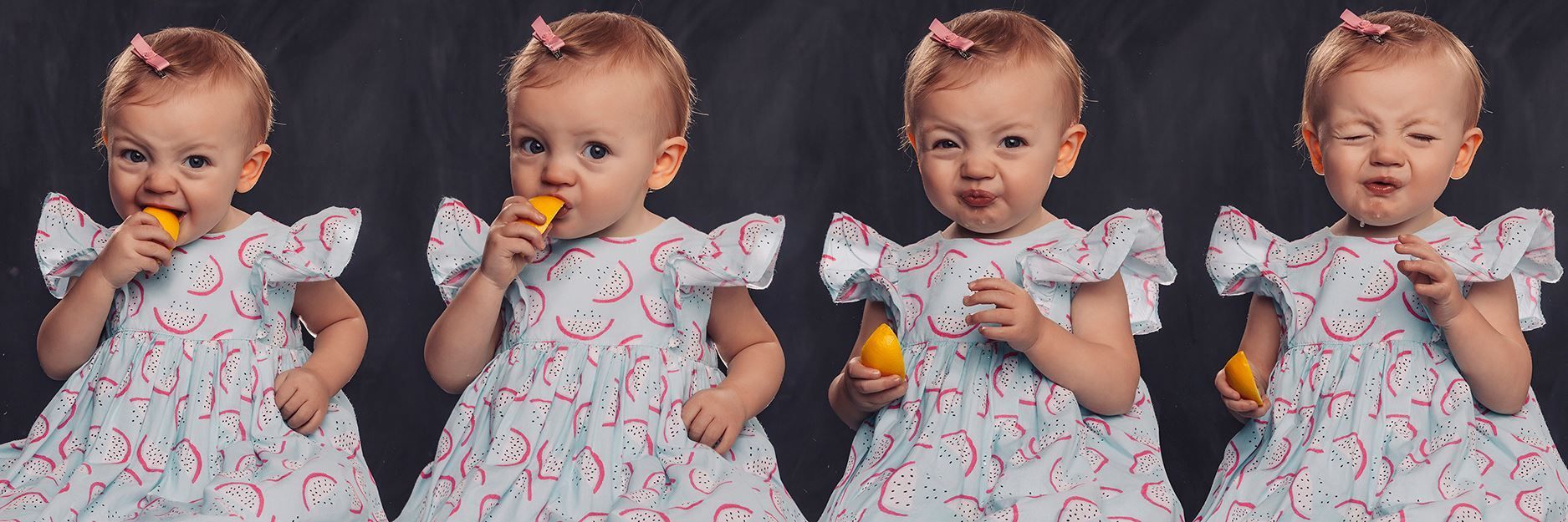 A little girl in a dress is eating a lemon.