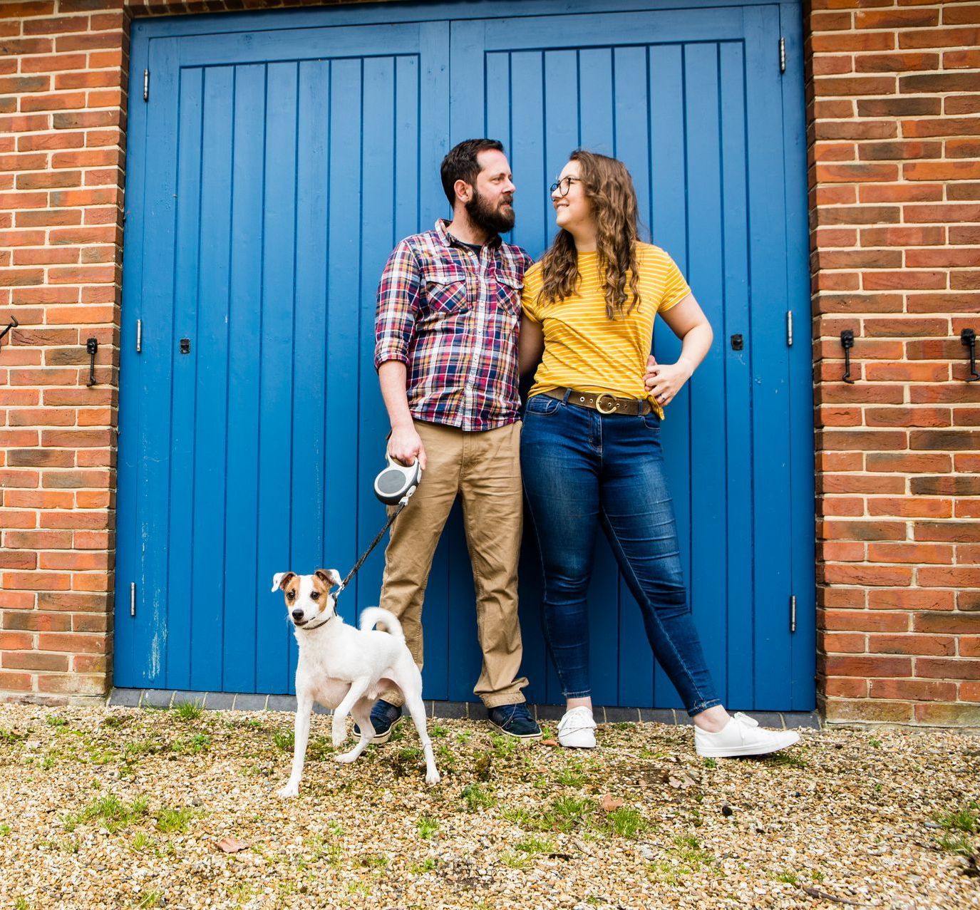 A man and woman standing next to a dog in front of a blue garage door.