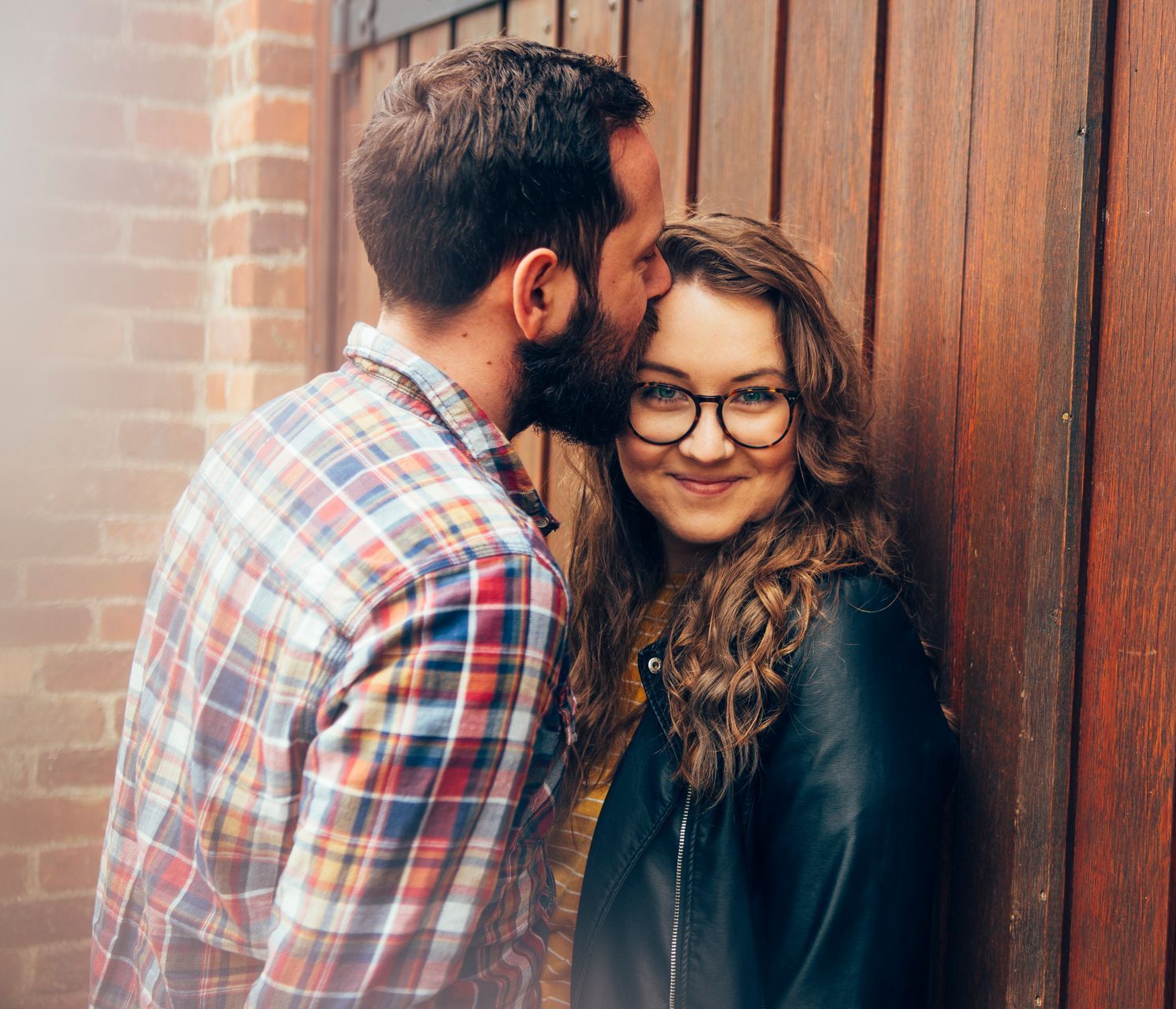 A man is kissing a woman on the forehead in front of a wooden door.