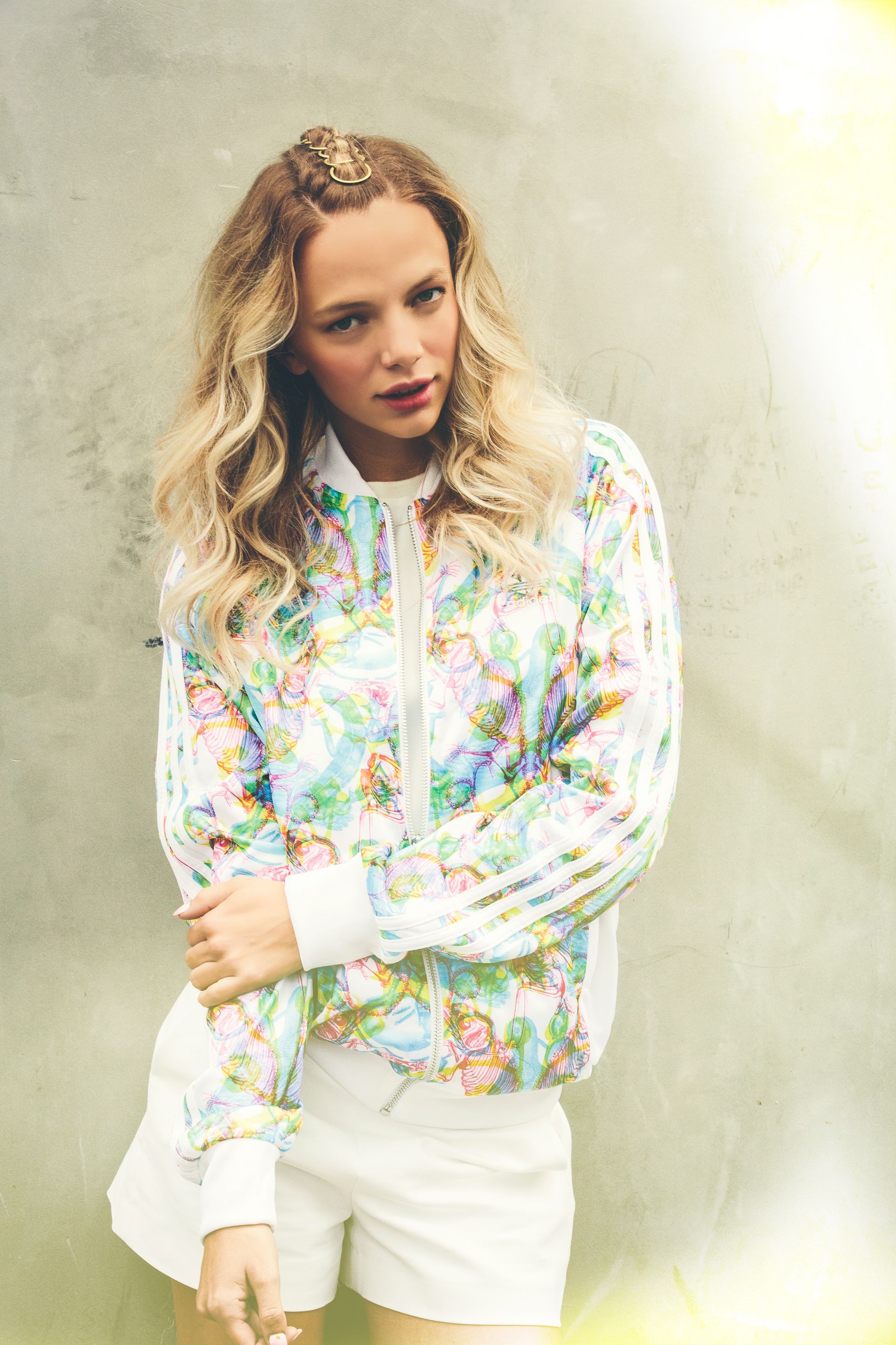 A woman wearing a floral jacket and white shorts is standing in front of a wall.