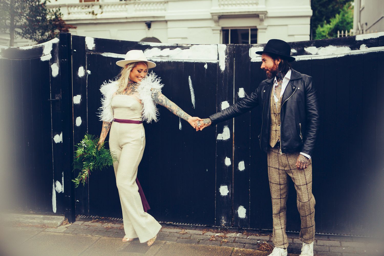 A bride and groom are holding hands in front of a black fence.