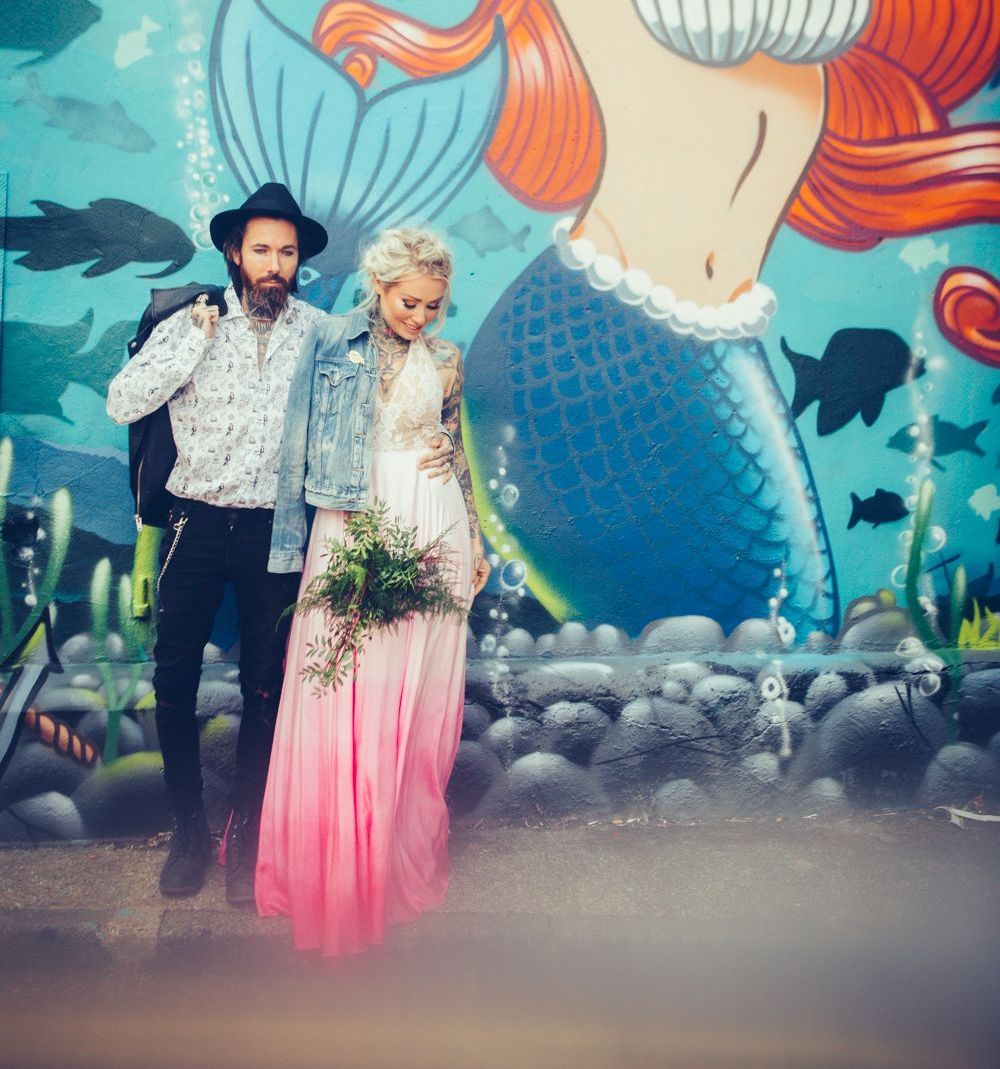 A man and woman are standing in front of a mural of a mermaid.