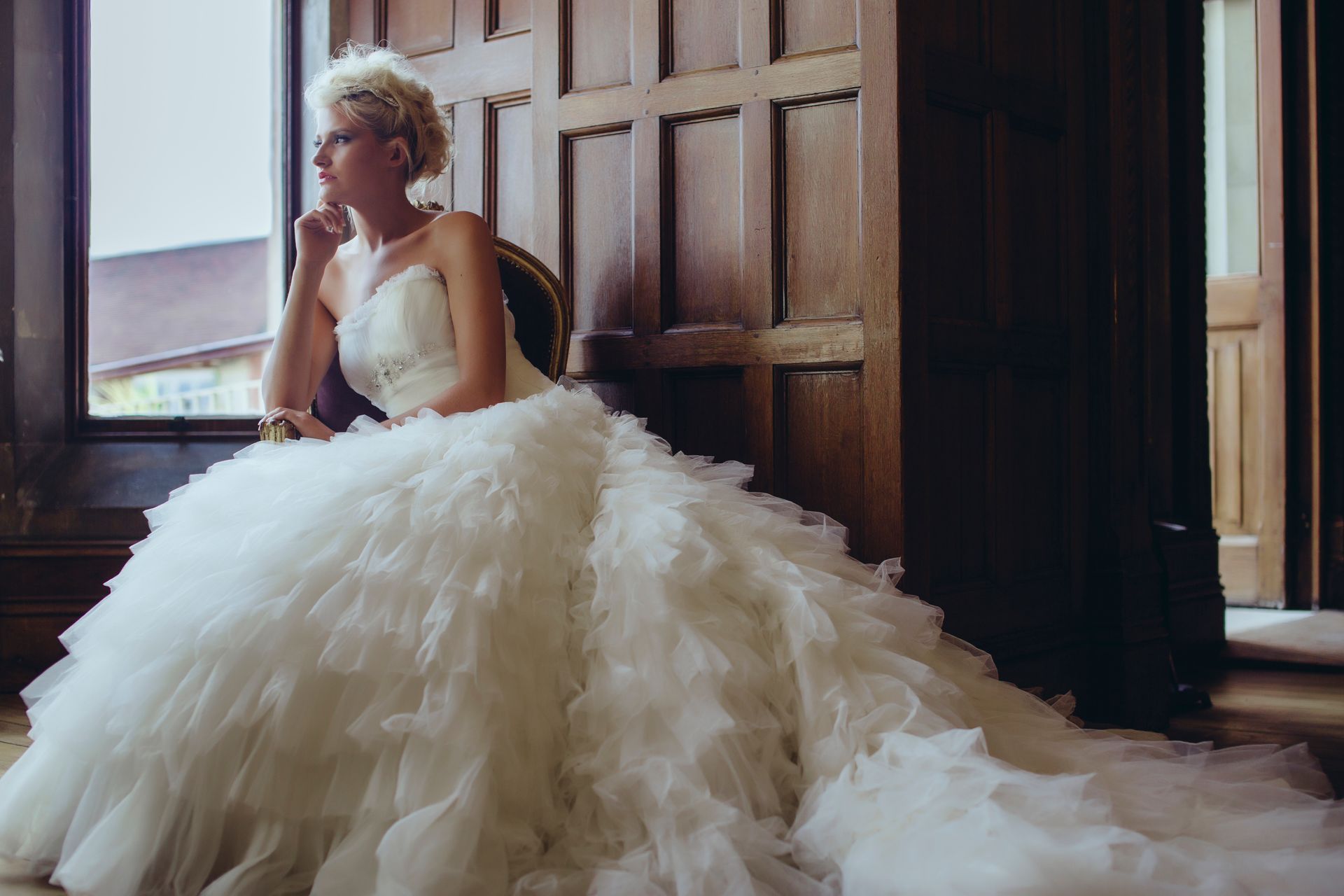 A woman in a wedding dress is sitting in a chair in front of a window.