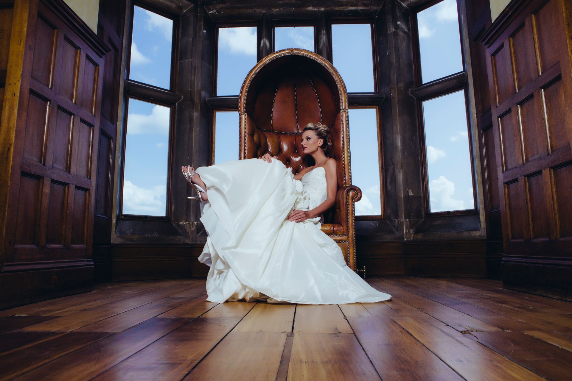 A woman in a wedding dress is sitting in a chair in front of a window.