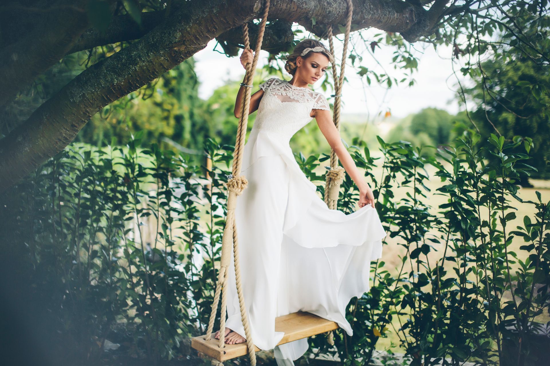 A woman in a wedding dress is sitting on a swing in a tree.