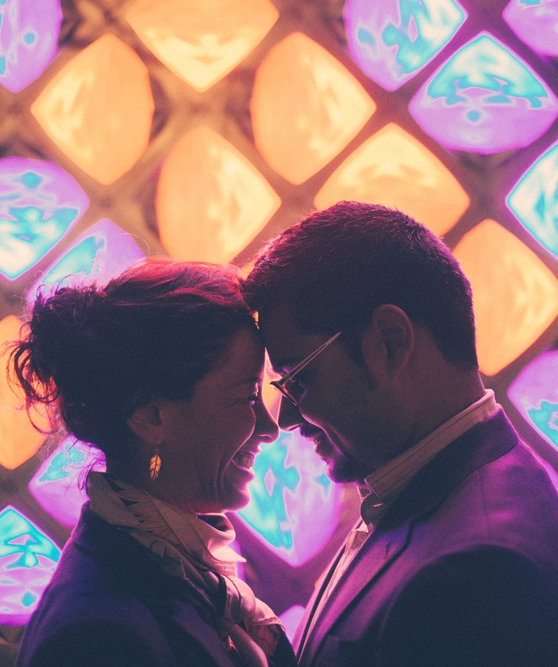 A man and a woman are looking at each other in front of a stained glass window.