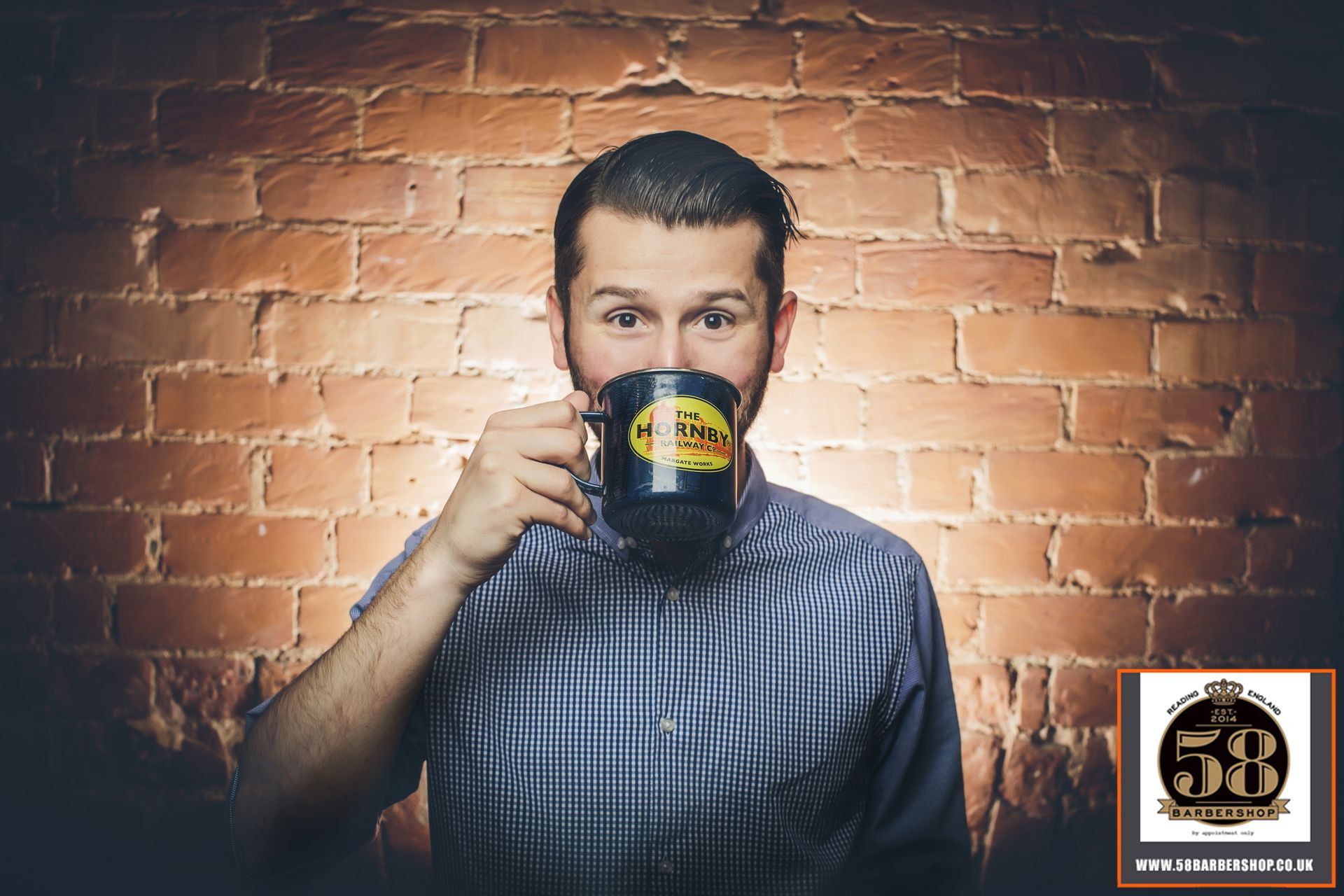 A man is drinking a cup of coffee in front of a brick wall.