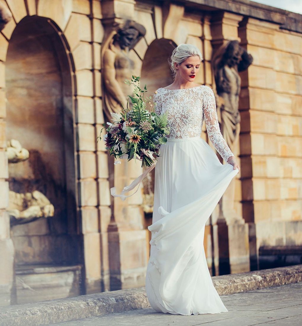 A woman in a white dress is holding a bouquet of flowers in front of a building.