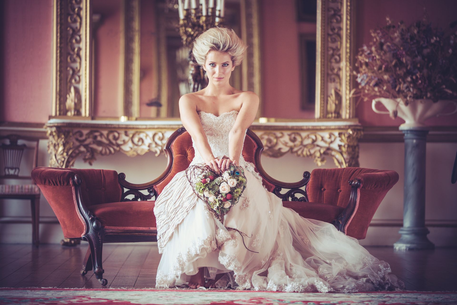 A woman in a wedding dress is sitting on a couch holding a bouquet of flowers.