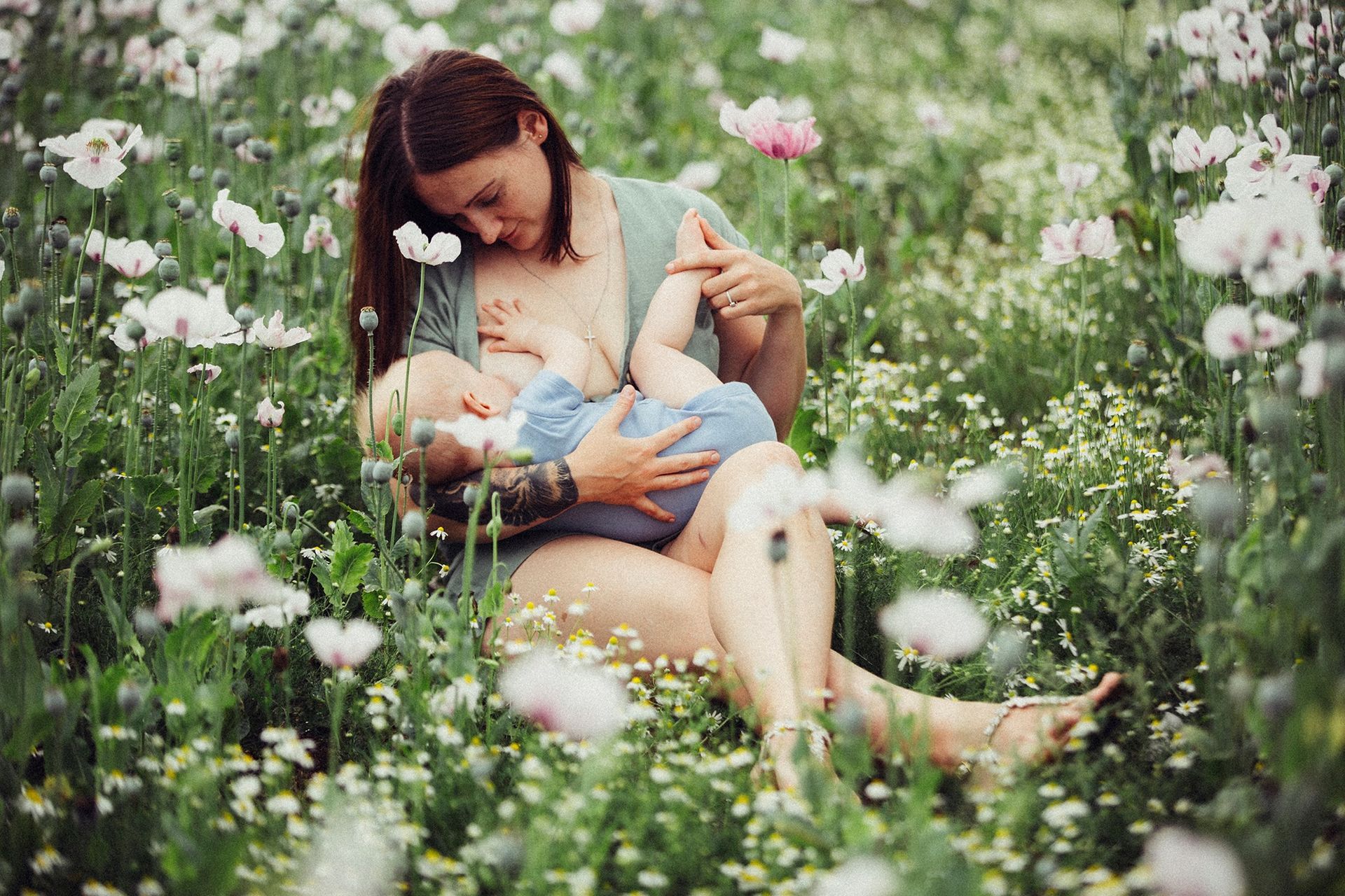 A woman is breastfeeding her baby in a field of flowers.