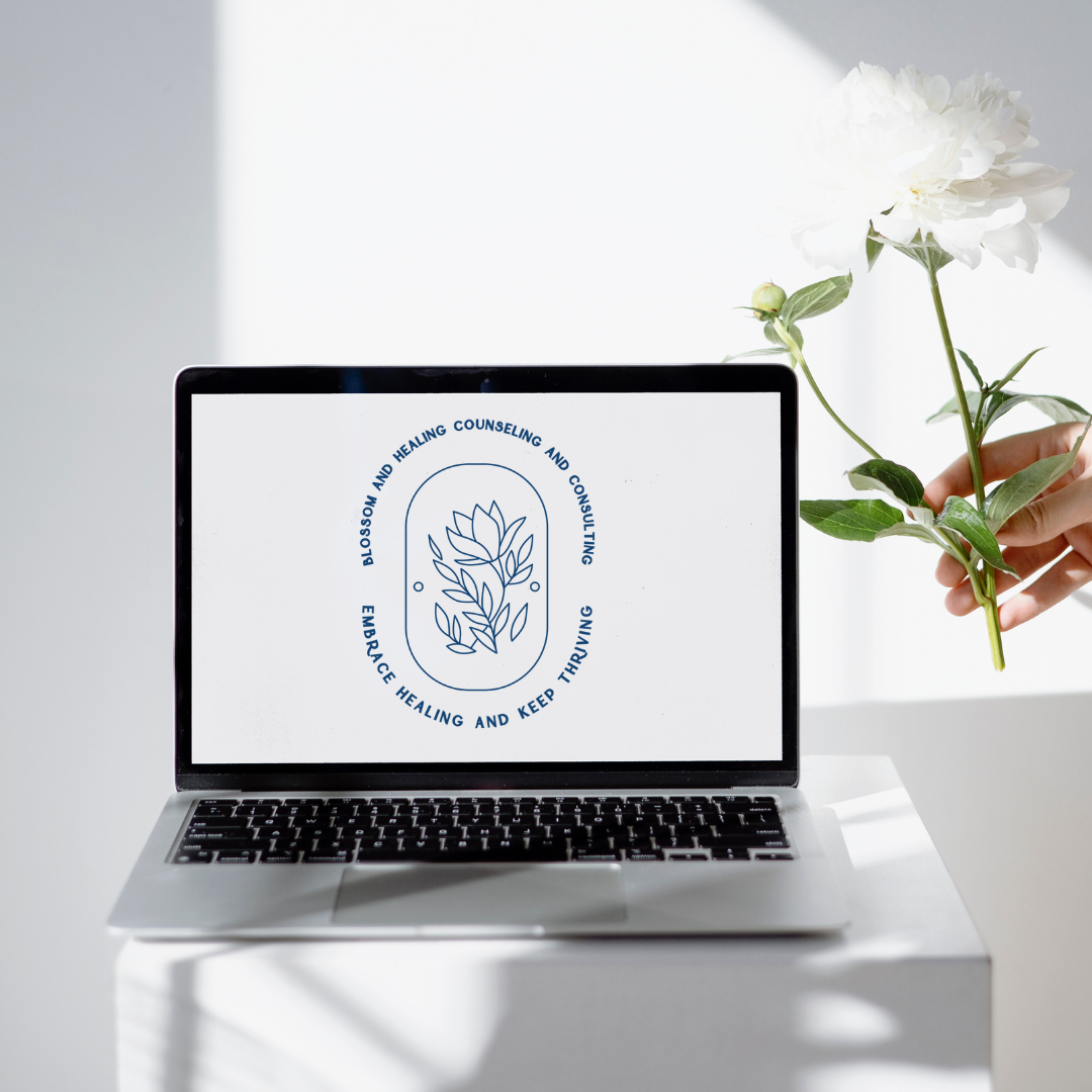Laptop with floral logo on a white surface, hand holding a white flower.