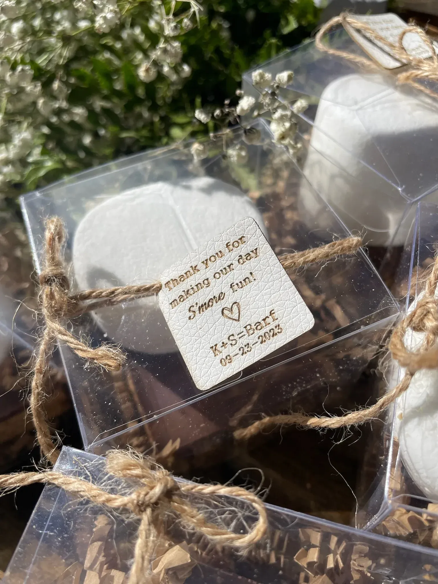 Clear favor boxes tied with twine, each holding a white item and a tag that reads 