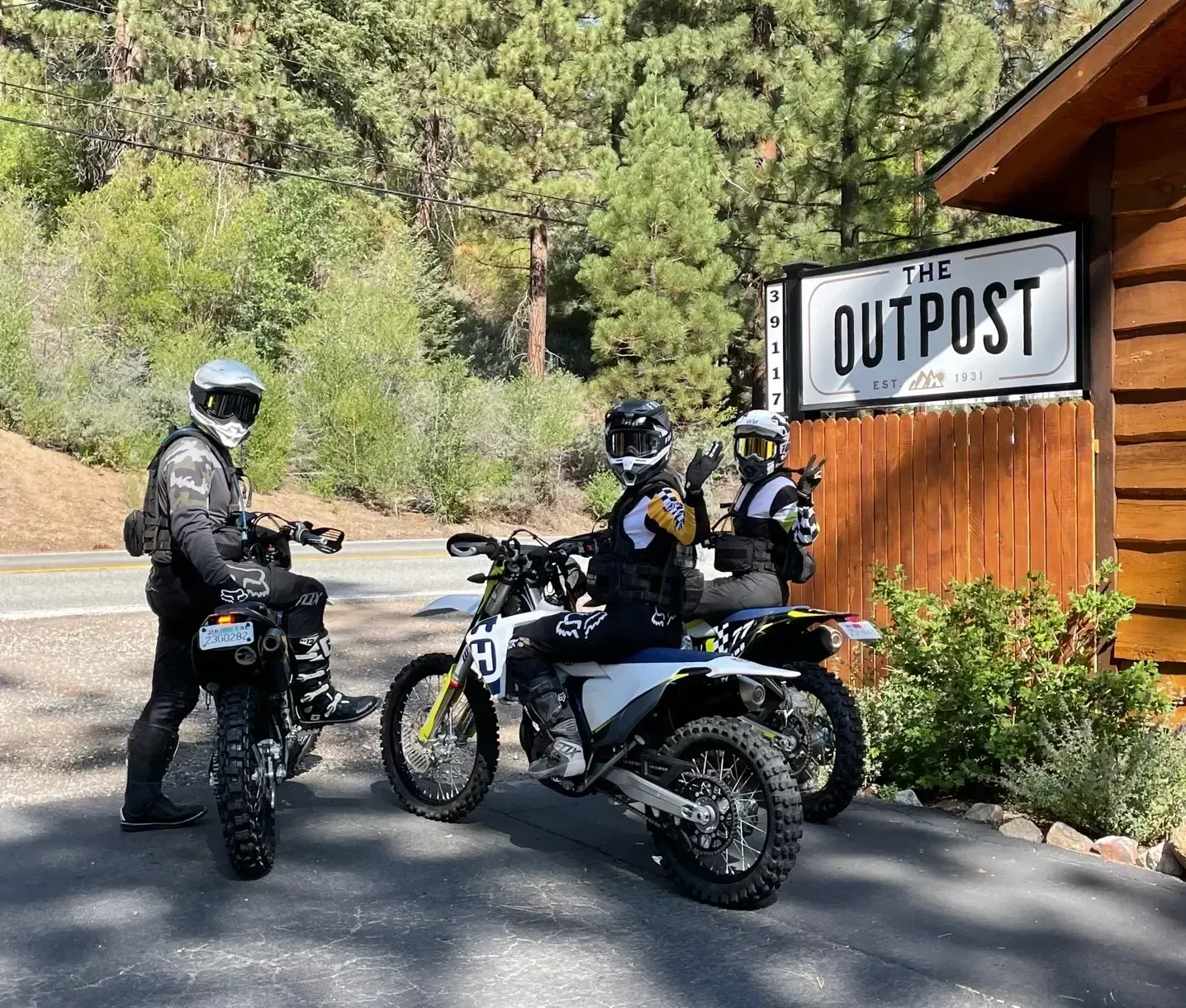 Three motorcyclists in gear pose near a sign that reads