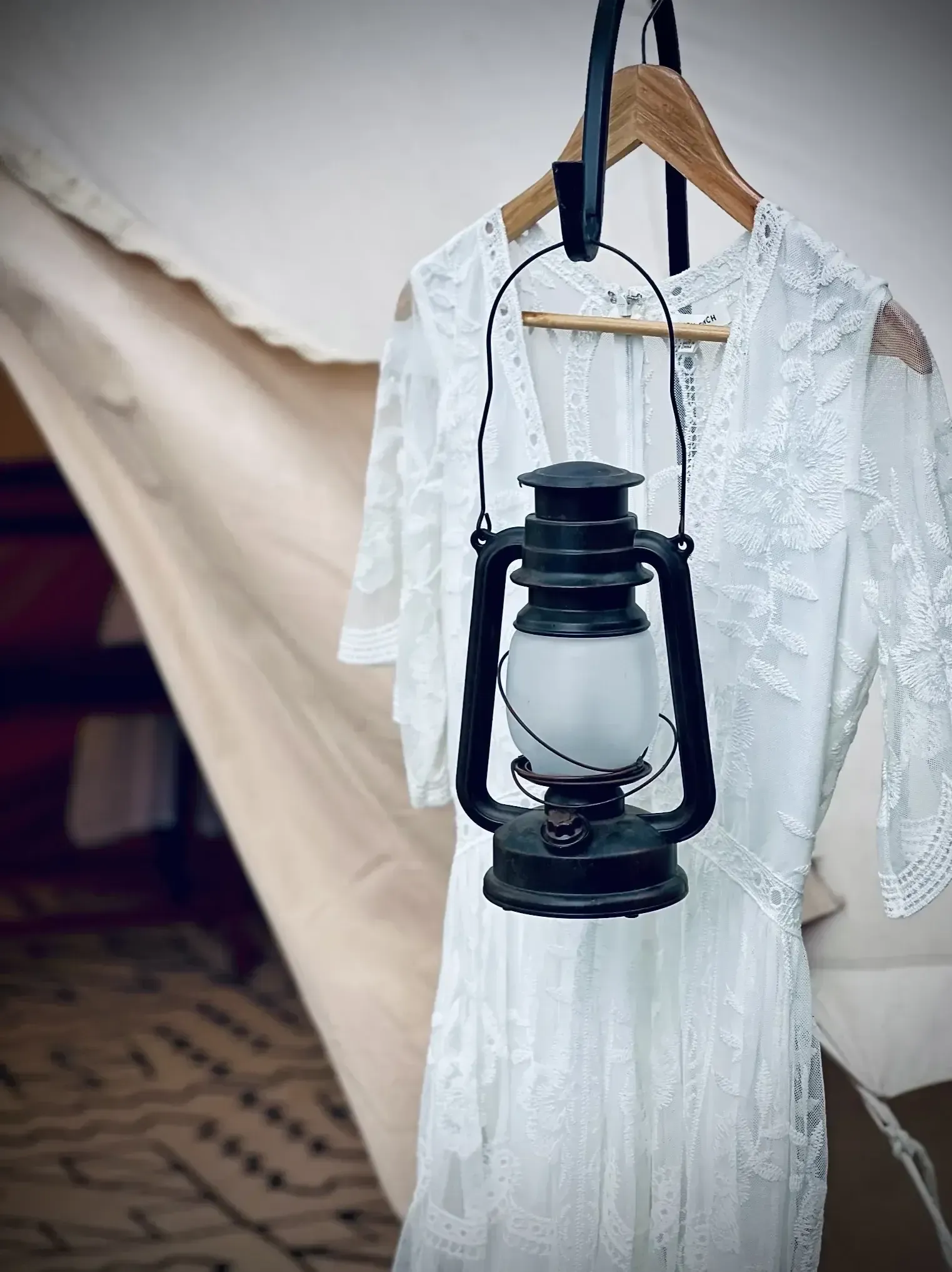 White lace dress hanging with a black lantern on a wood hanger in a tent.