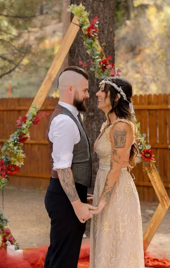 Couple holding hands, smiling, at an outdoor wedding ceremony under a floral arch.
