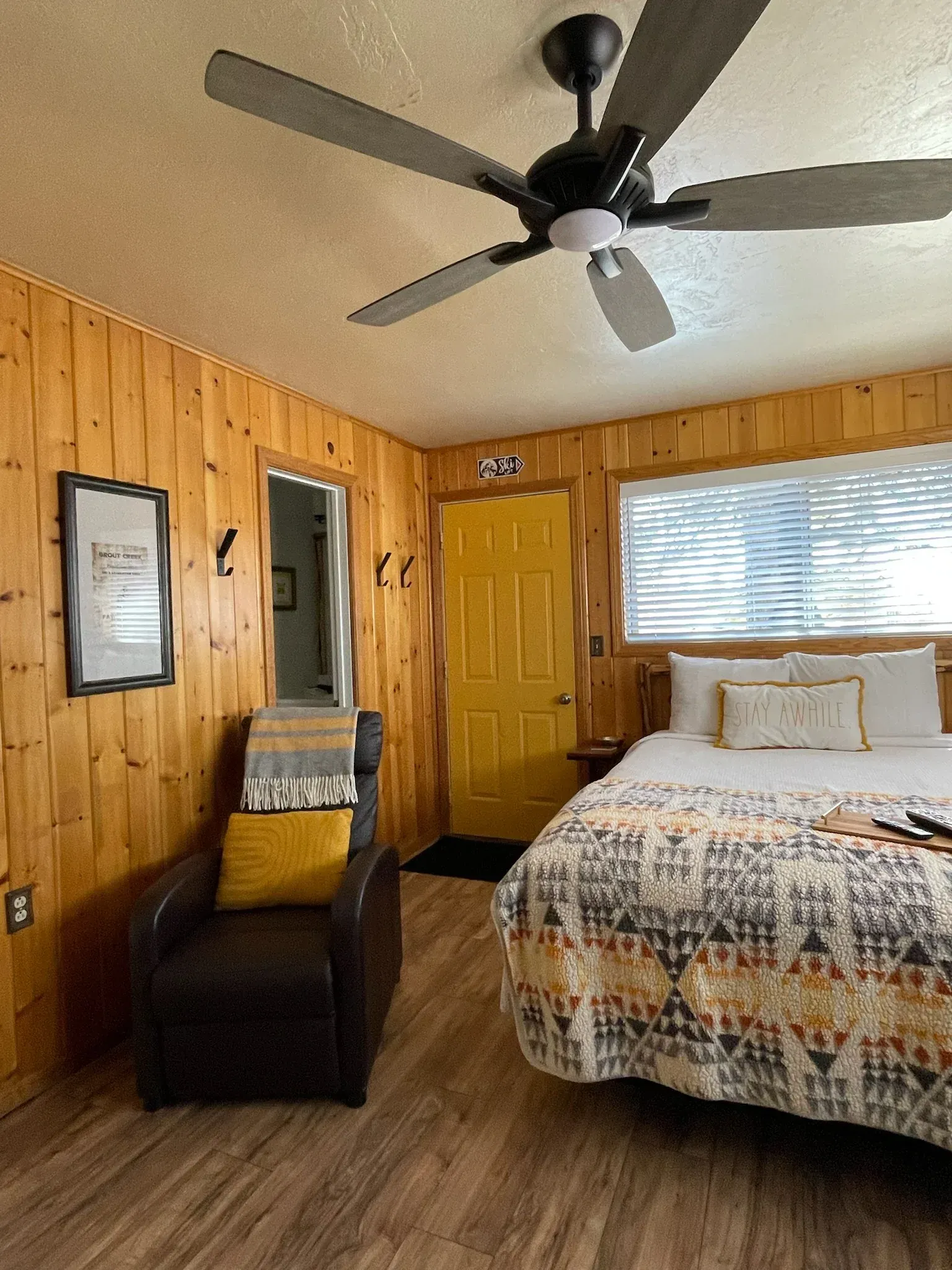 Bedroom with wood paneling, a yellow door, bed, chair, and ceiling fan.