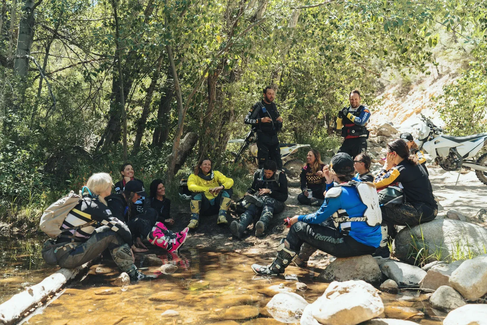 Group of people in outdoor gear gathered by a stream, listening to someone.