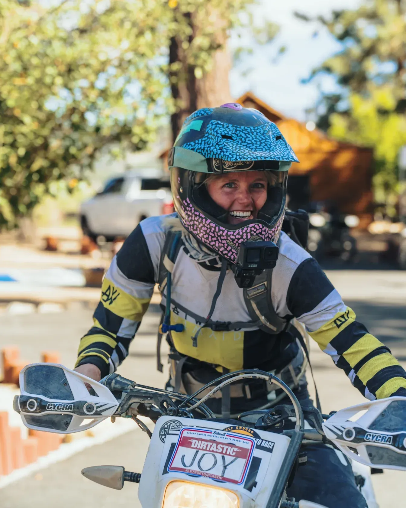 Woman on motorcycle, wearing helmet, smiling. Outdoor setting.