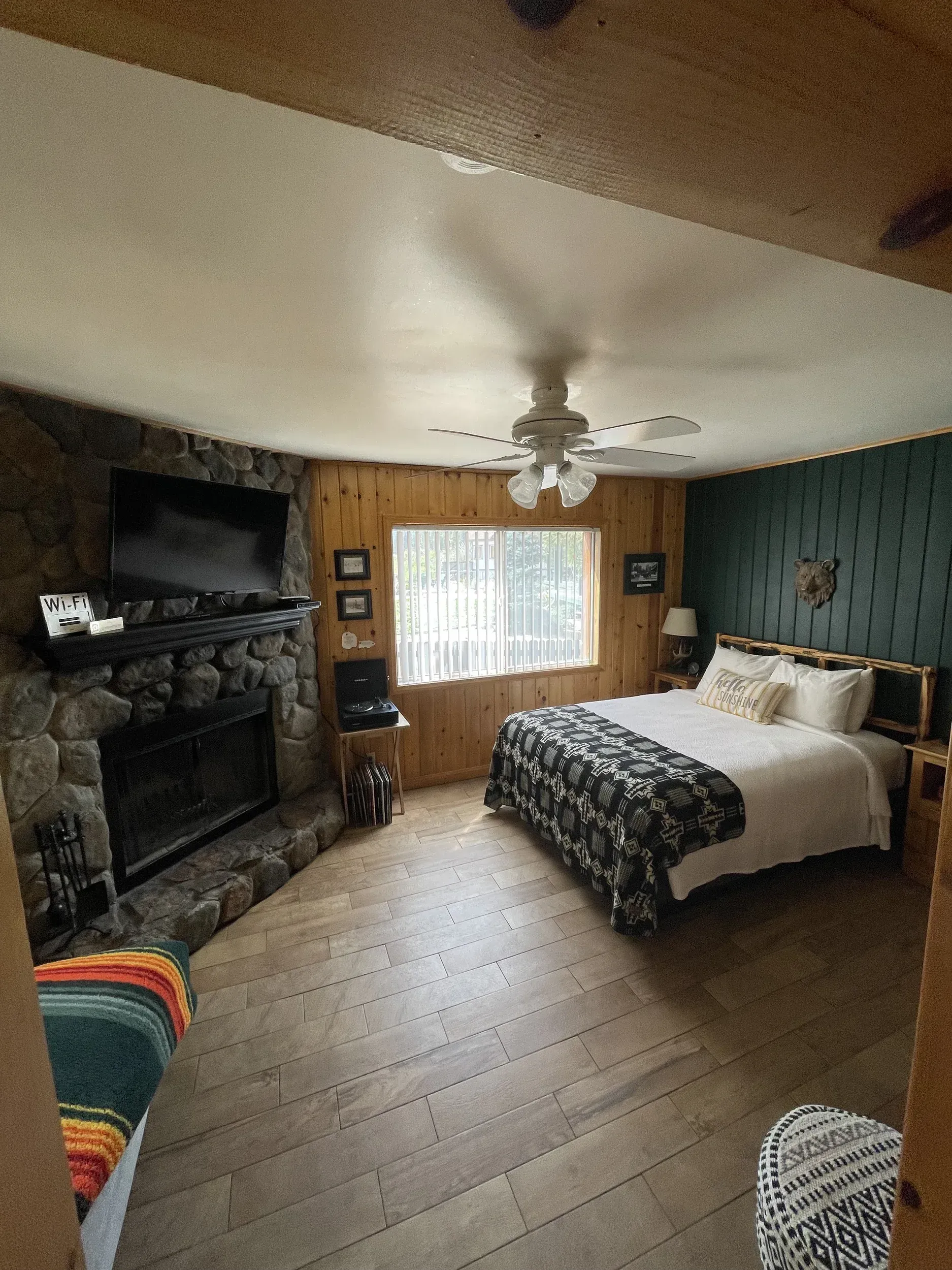 Bedroom with fireplace, bed, and window. Fireplace is stone. Walls are wood and green.