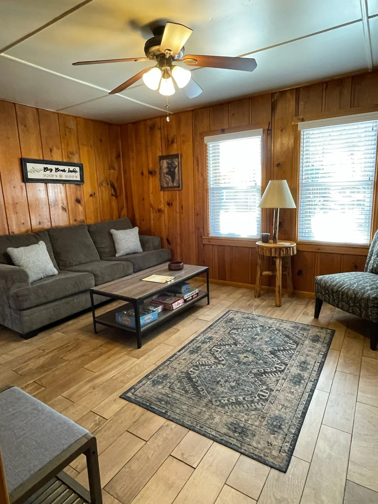 Living room with wood paneling, couch, area rug, windows, and ceiling fan.