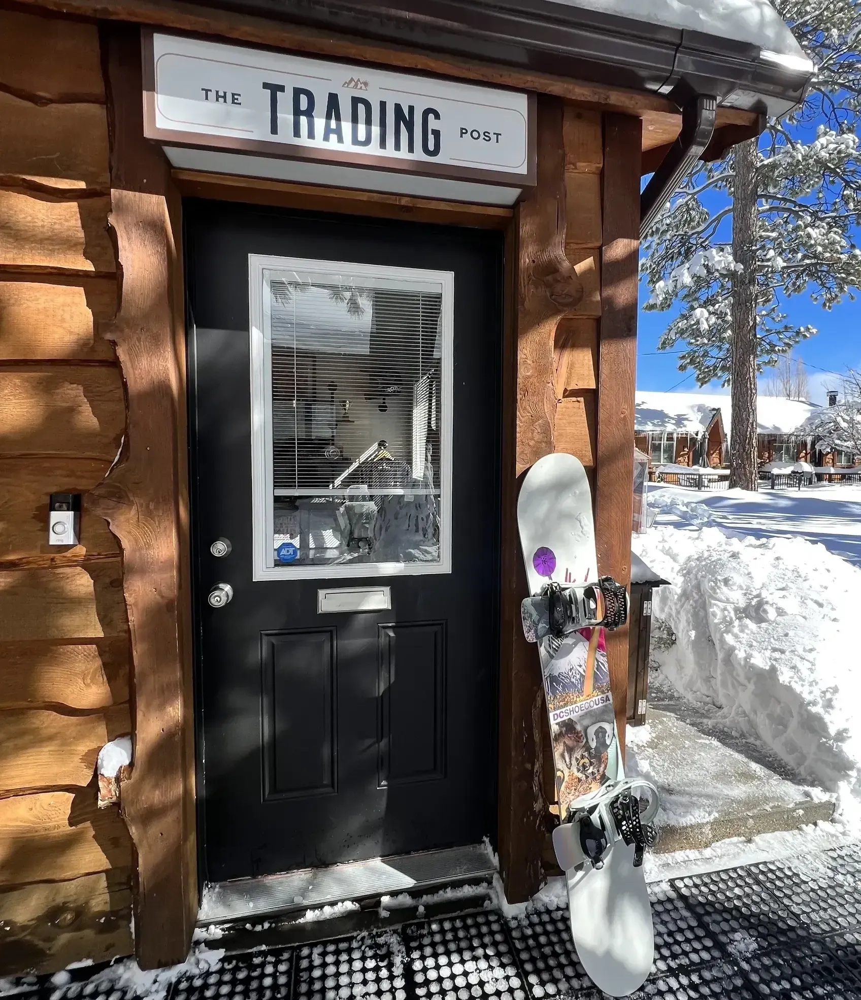 The Trading Co. storefront with a snowboard leaning against the door in a snowy setting.