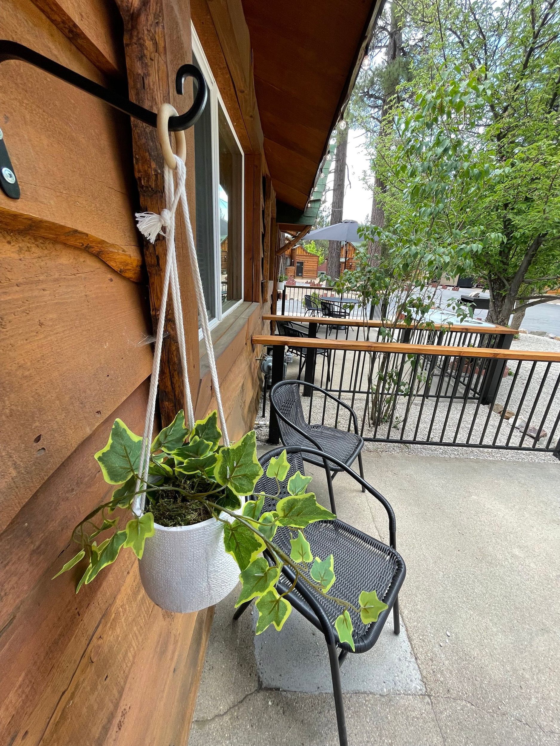 Hanging plant in a white pot on a porch.  Wicker chairs and railings on the right. Wooden building.