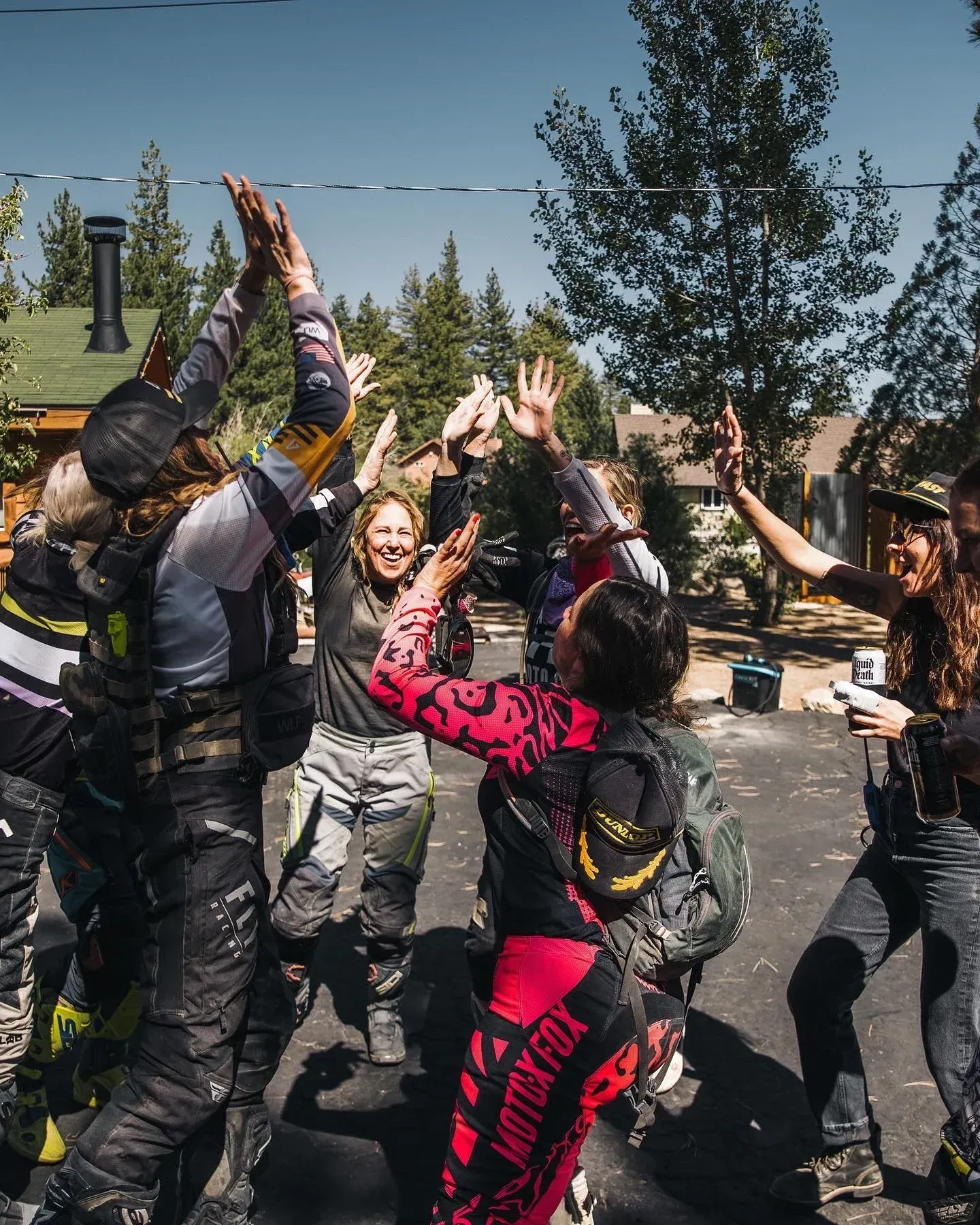 Group of motorcyclists celebrating with high fives outdoors.