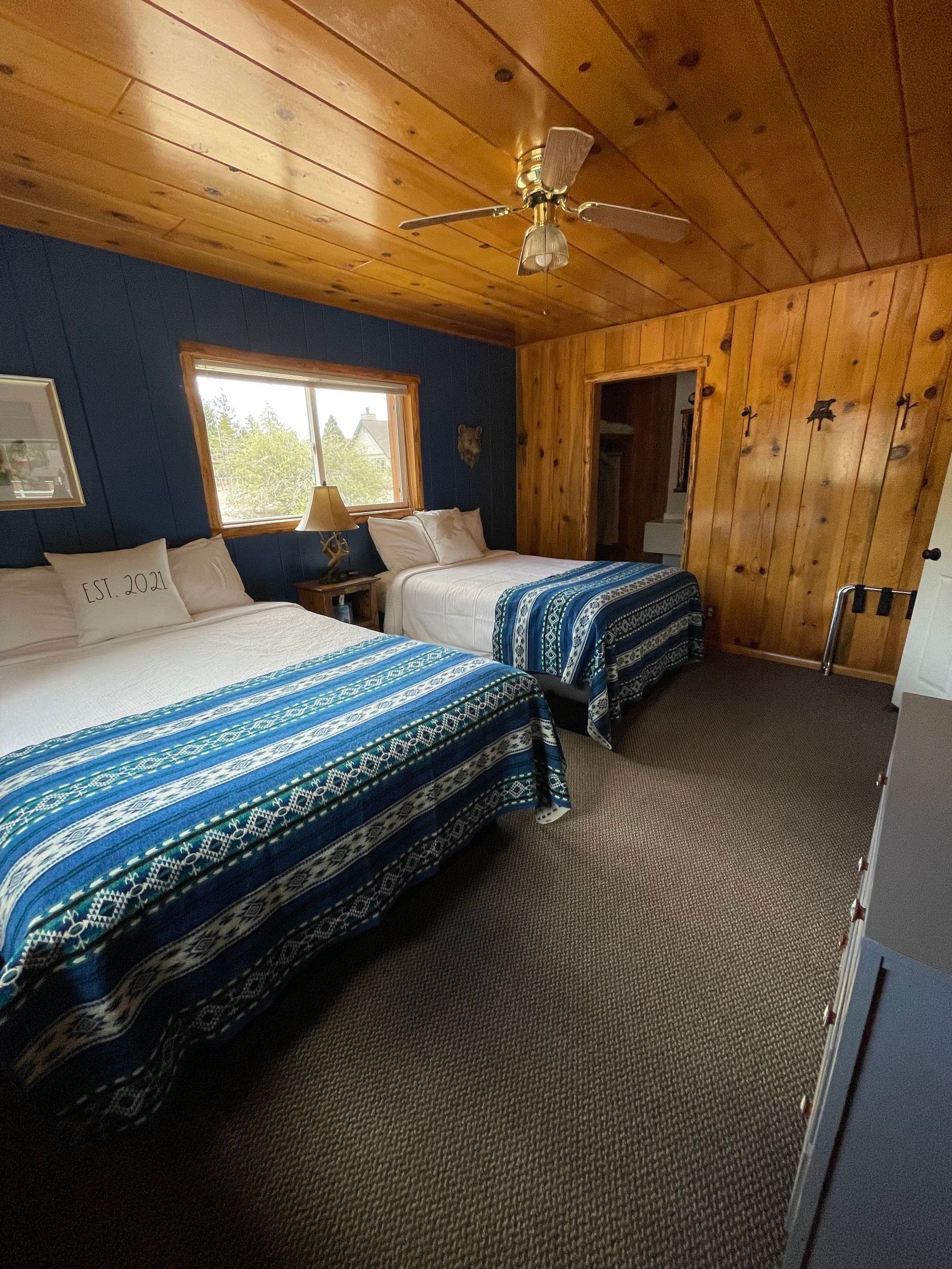 Bedroom with two beds, blue and white blankets, wood paneling, and a window.