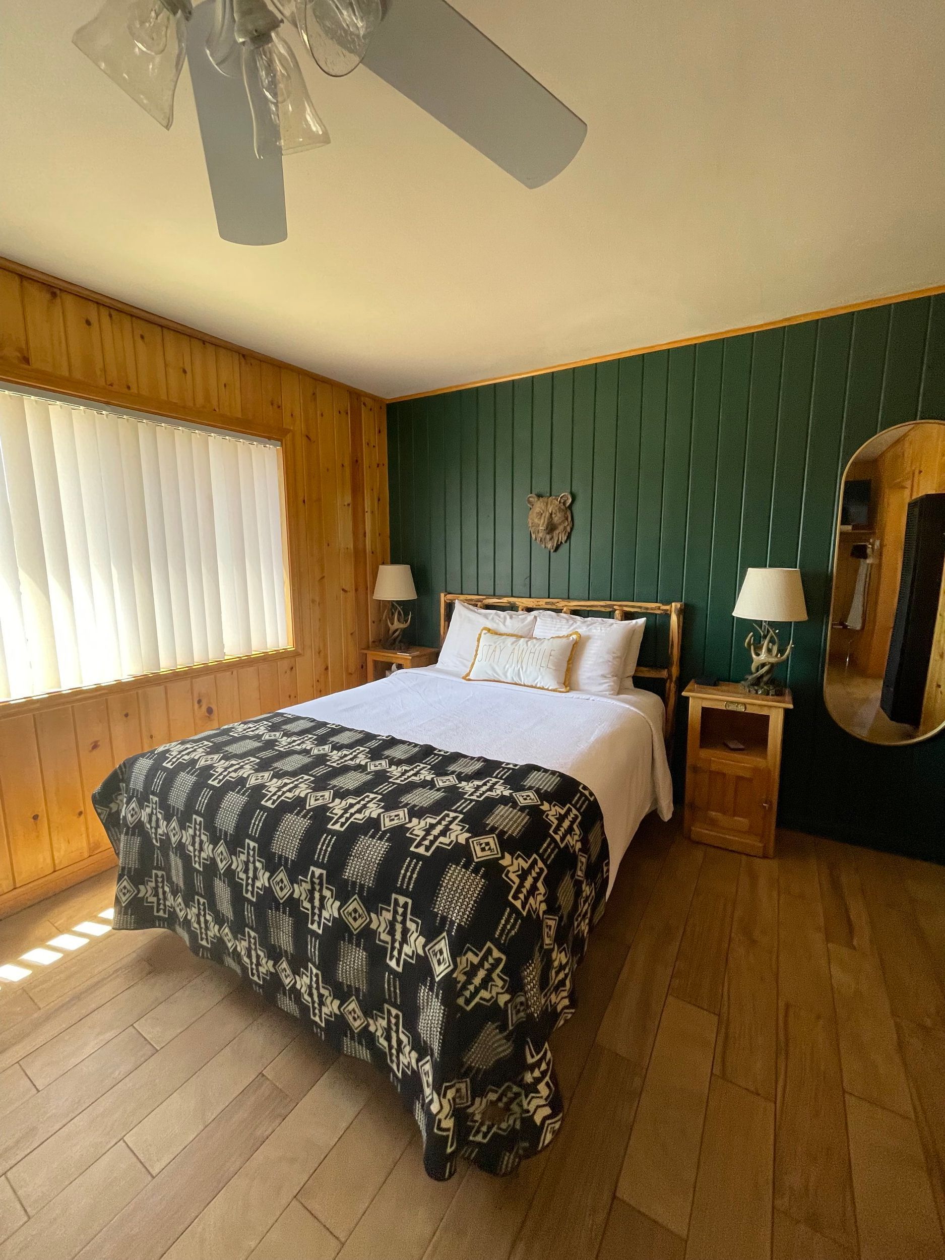 Bedroom with bed, dark floral blanket, wood paneling, green accent wall, and mirror.