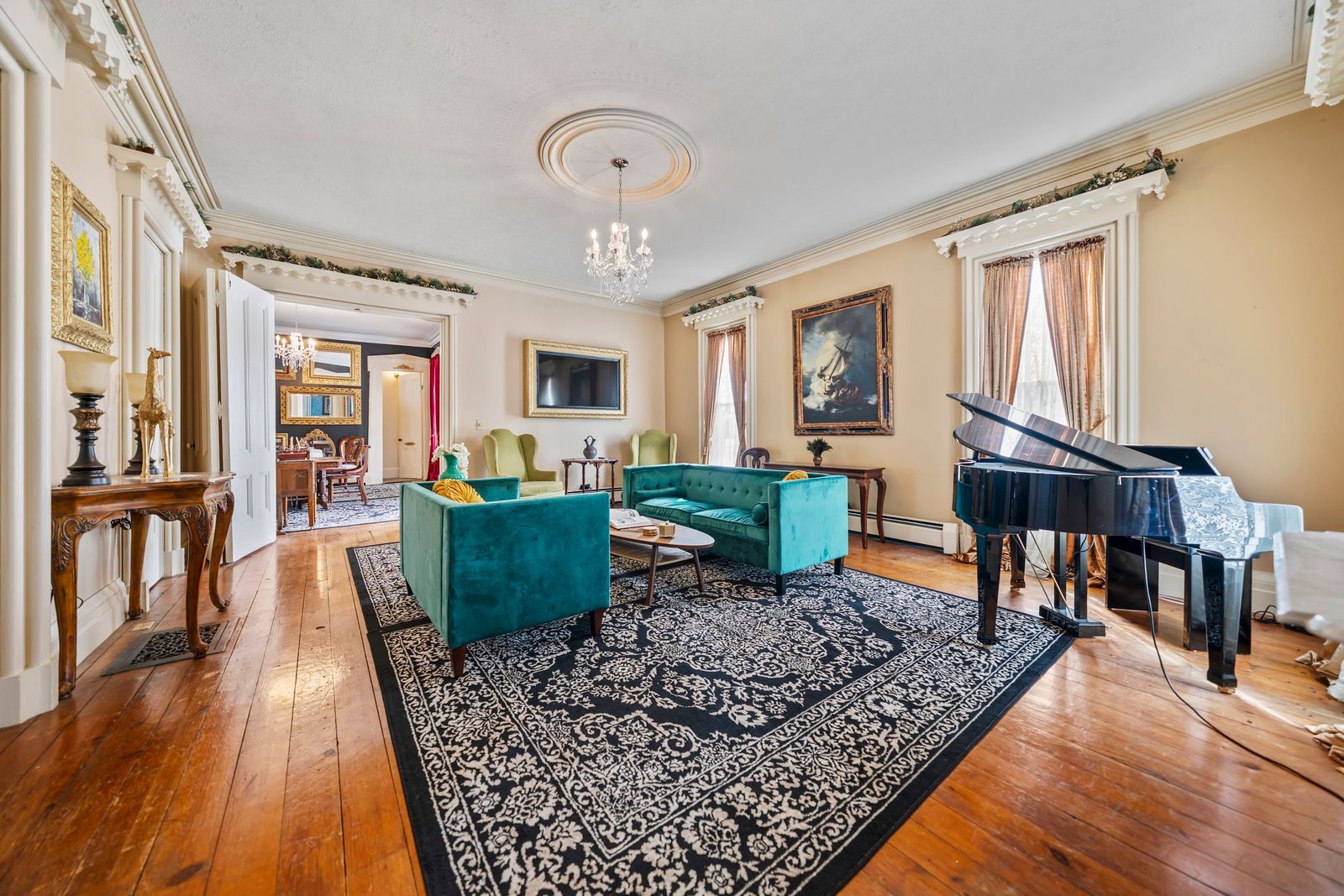 A formal living room with two green sofas, a black grand piano, and a large patterned rug on hardwood floors.